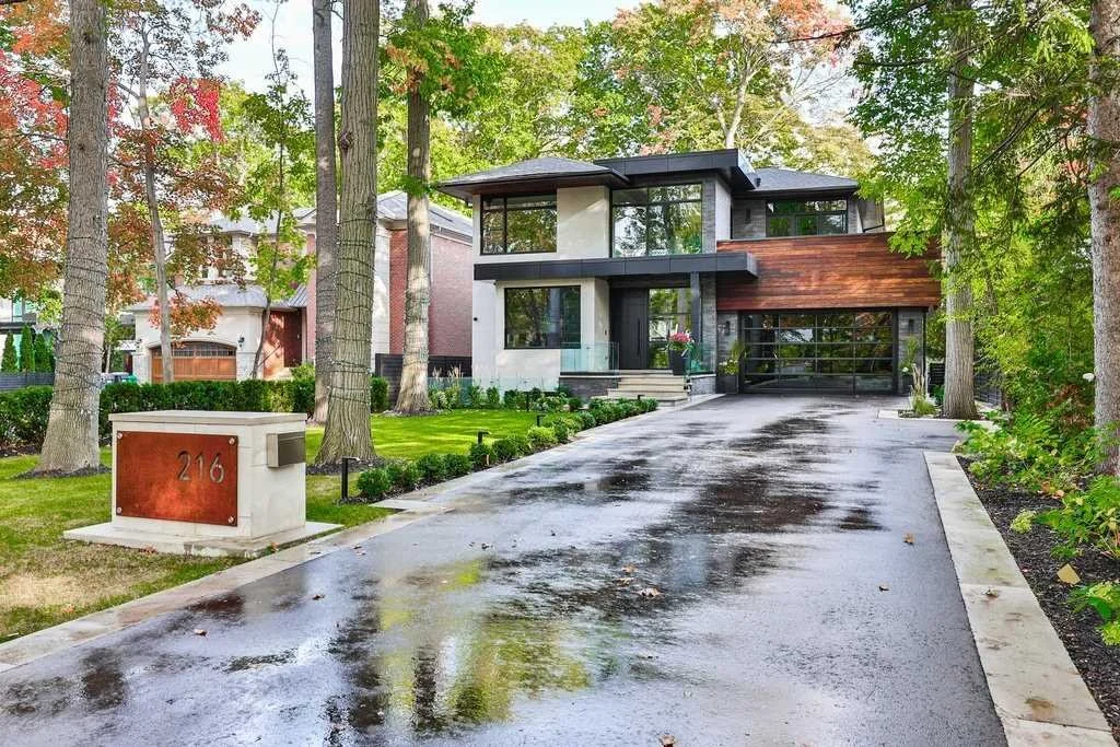 Modern house with a garage, driveway, and landscaped yard with trees and bushes, on a rainy day.