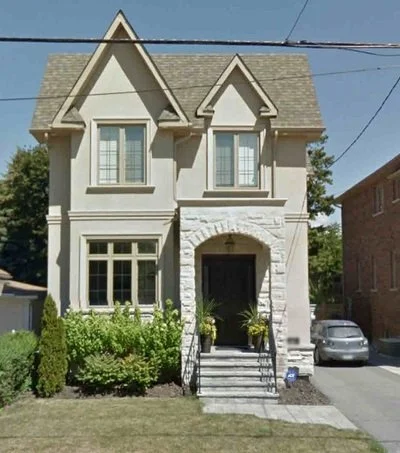 Front view of a two-story house with a stone entryway, multiple windows, and a small front garden with bushes.