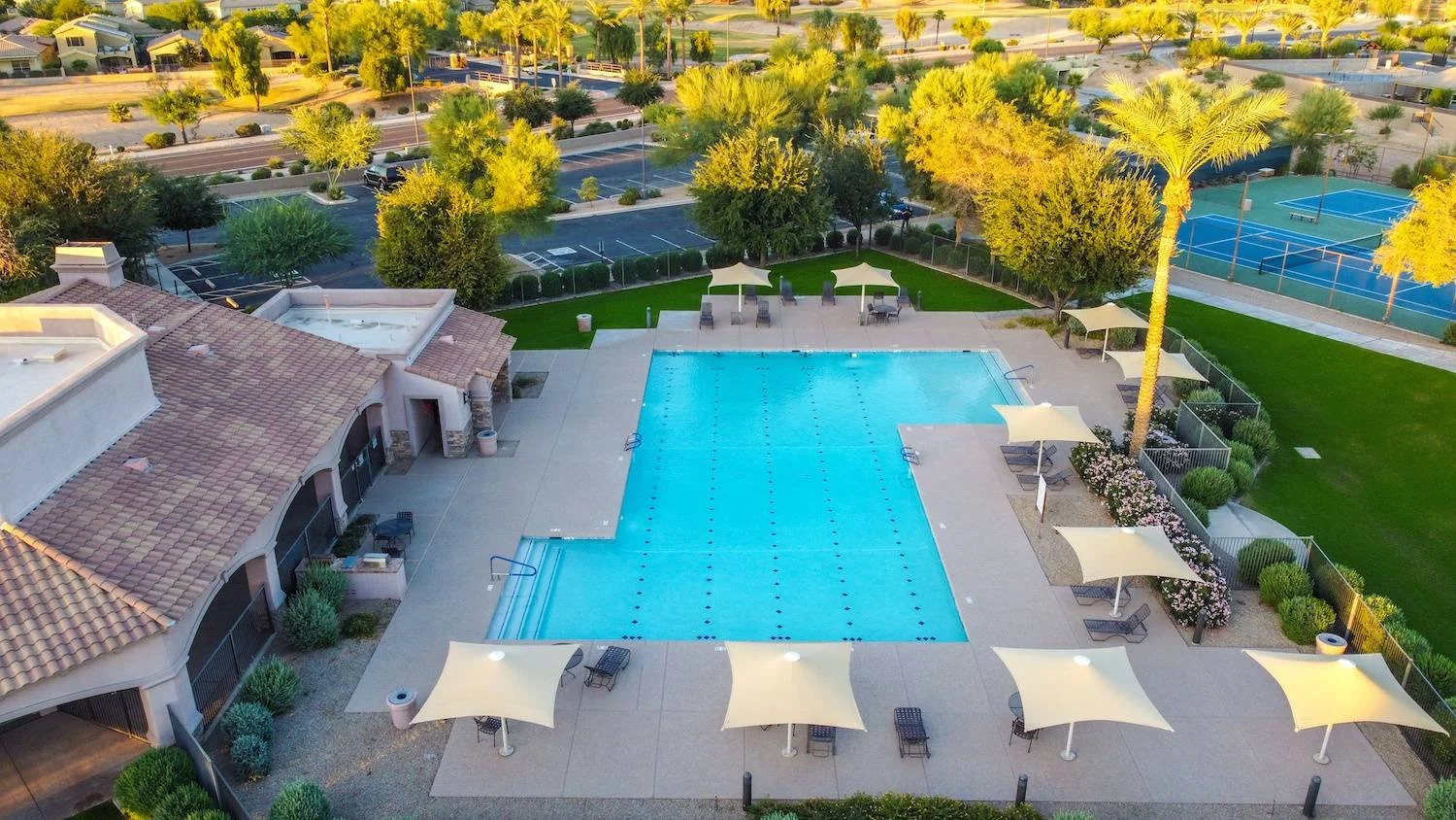 Aerial view of a community clubhouse with resort-style pool, tennis courts, landscaped common areas, and maintained HOA grounds