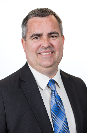 Portrait of a man in a suit and tie smiling against a white background.