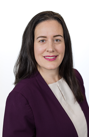 Professional woman with long dark hair wearing a purple blazer and white top, smiling against a white background.