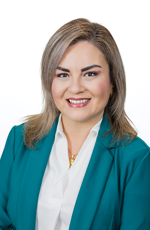 Professional woman with gray hair, smiling, wearing a white blouse and teal blazer, against a white background.
