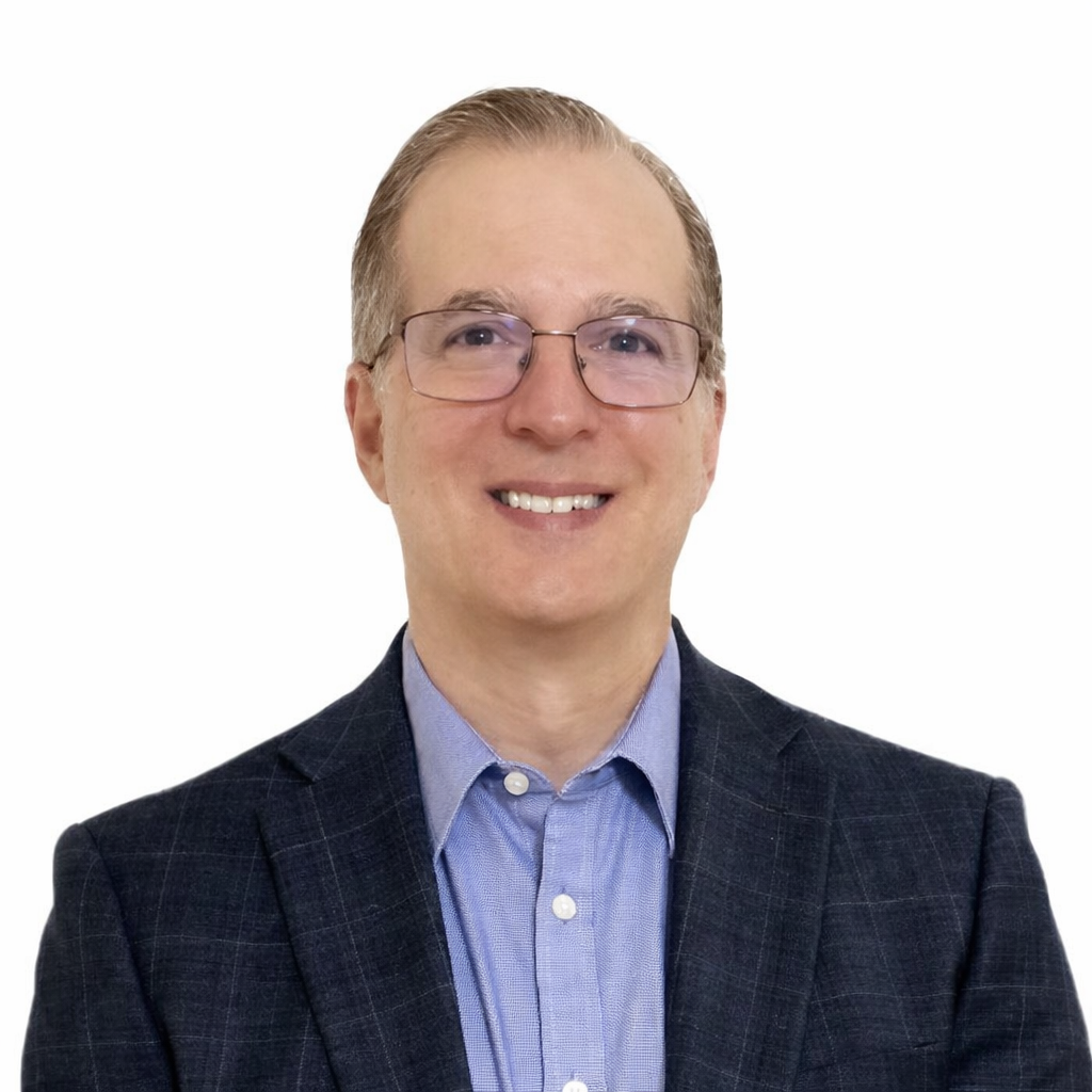 Headshot of a smiling man wearing glasses, a navy blazer, and a light blue shirt with a white background.