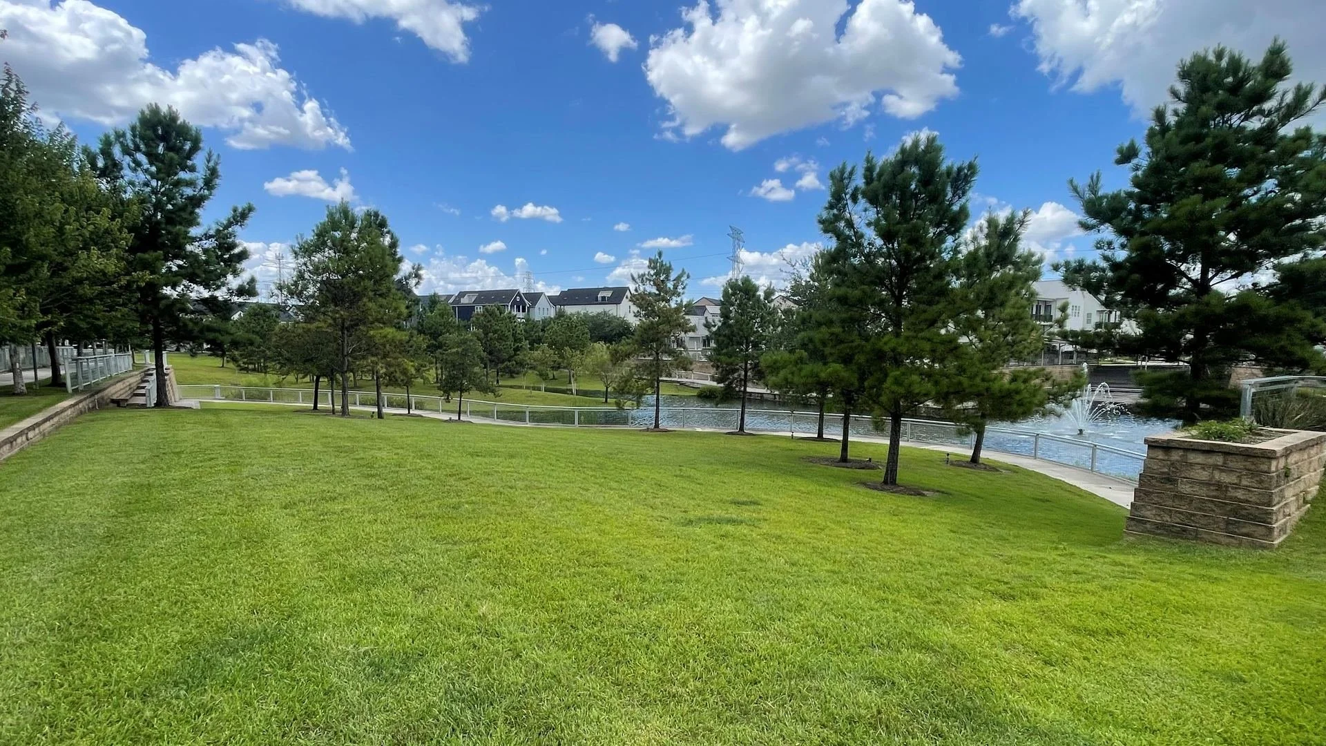 Green common-area lawn beside the Kolbe Farms retention pond with a fountain and pine trees. — Ethoscapes