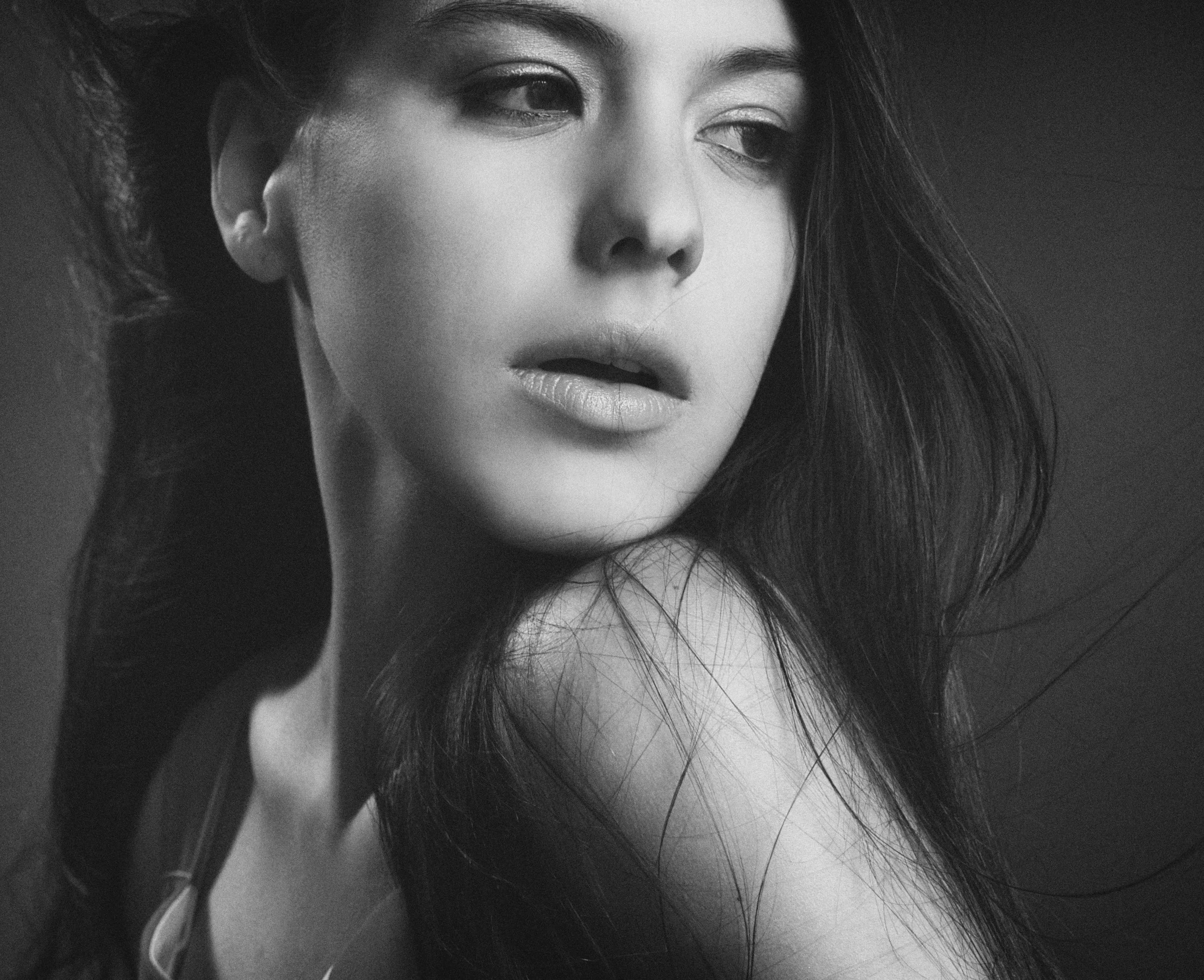 Black and white close-up portrait of a woman with long hair, looking to her left with her lips slightly parted.