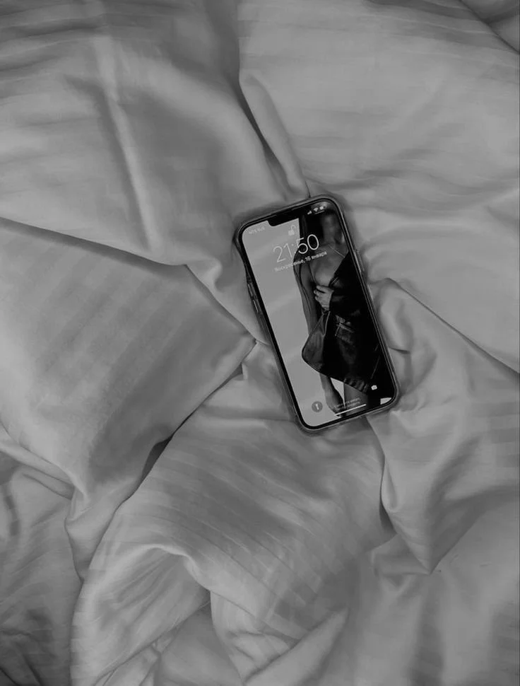 A smartphone lying on rumpled bedsheets, displaying the time 21:50 and a woman in a black outfit on the lock screen.