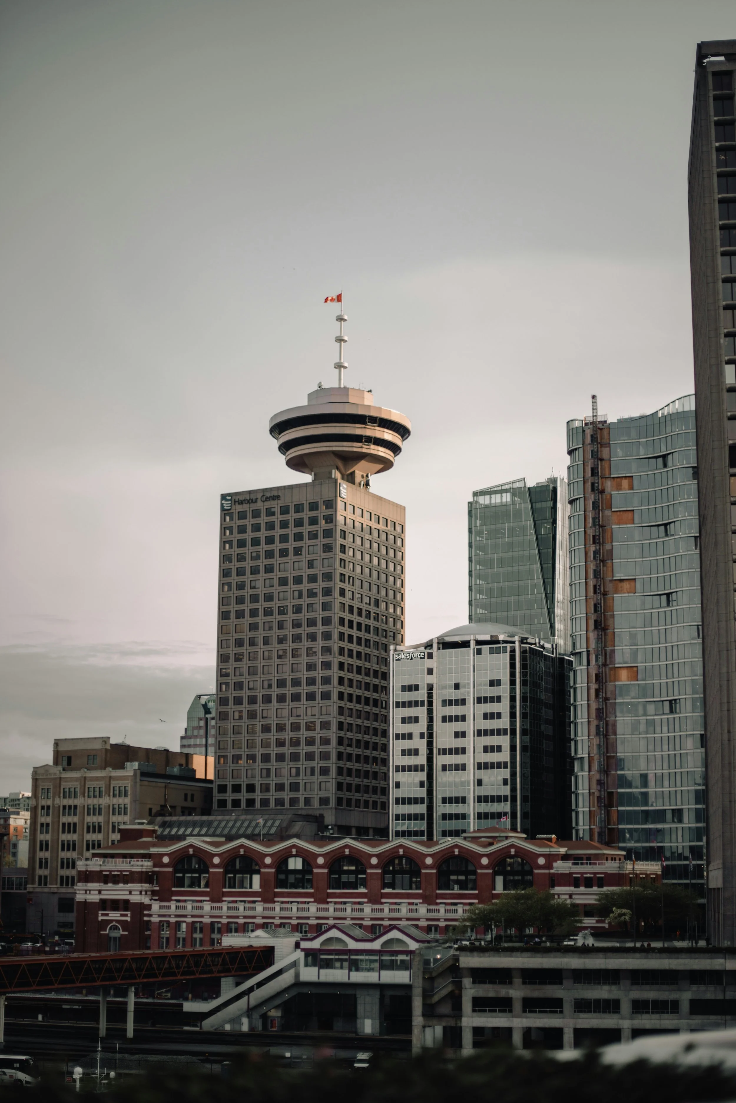 Skyline of downtown Vancouver, Canada with modern skyscrapers and the Harbour Centre building featuring a circular observation tower and a Canadian flag on top.