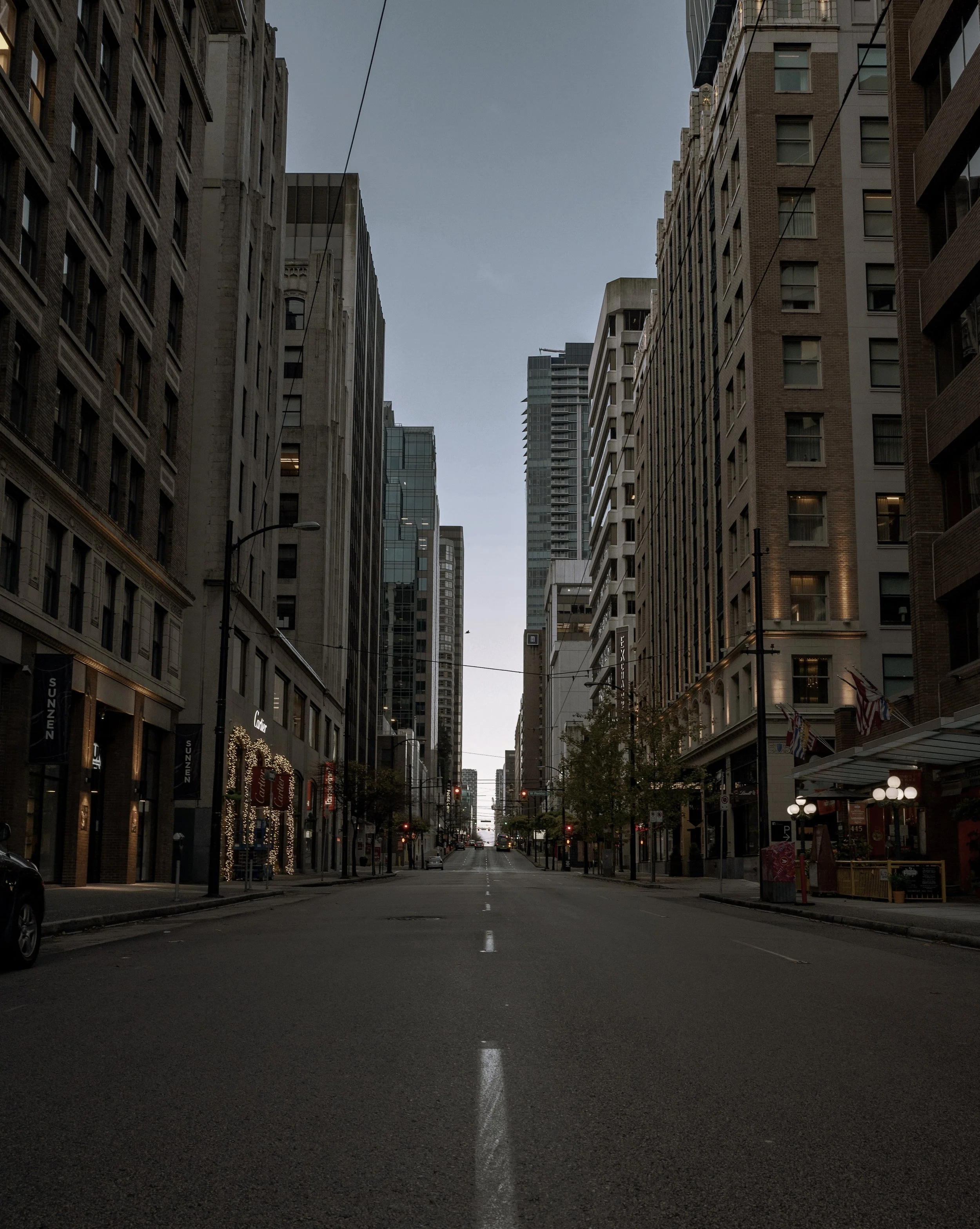 Empty city street lined with tall buildings on both sides, with some storefronts and flags, and a clear sky overhead.