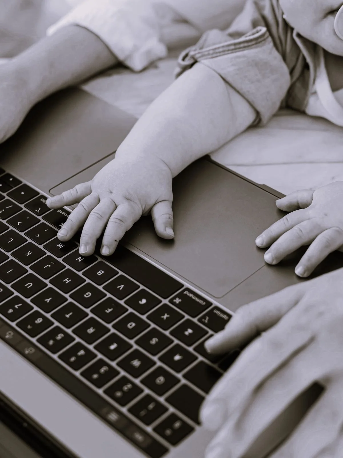 A child with small hands touching a laptop keyboard and trackpad.
