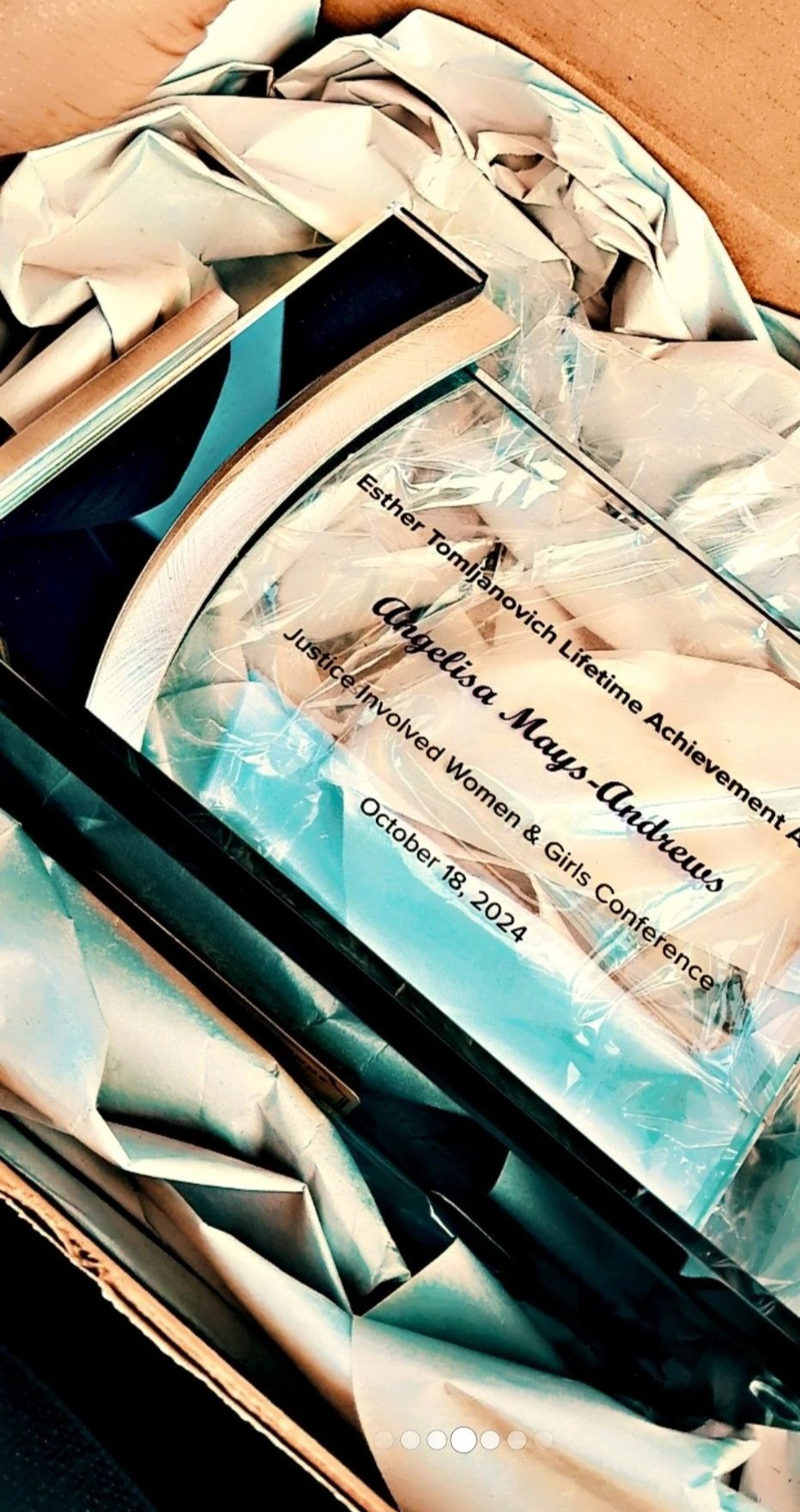 A framed certificate with the name 'Augustina Mays-Andrews' for the Justice Involved Women & Girls Conference on October 18, 2024, placed on crumpled paper inside a box.