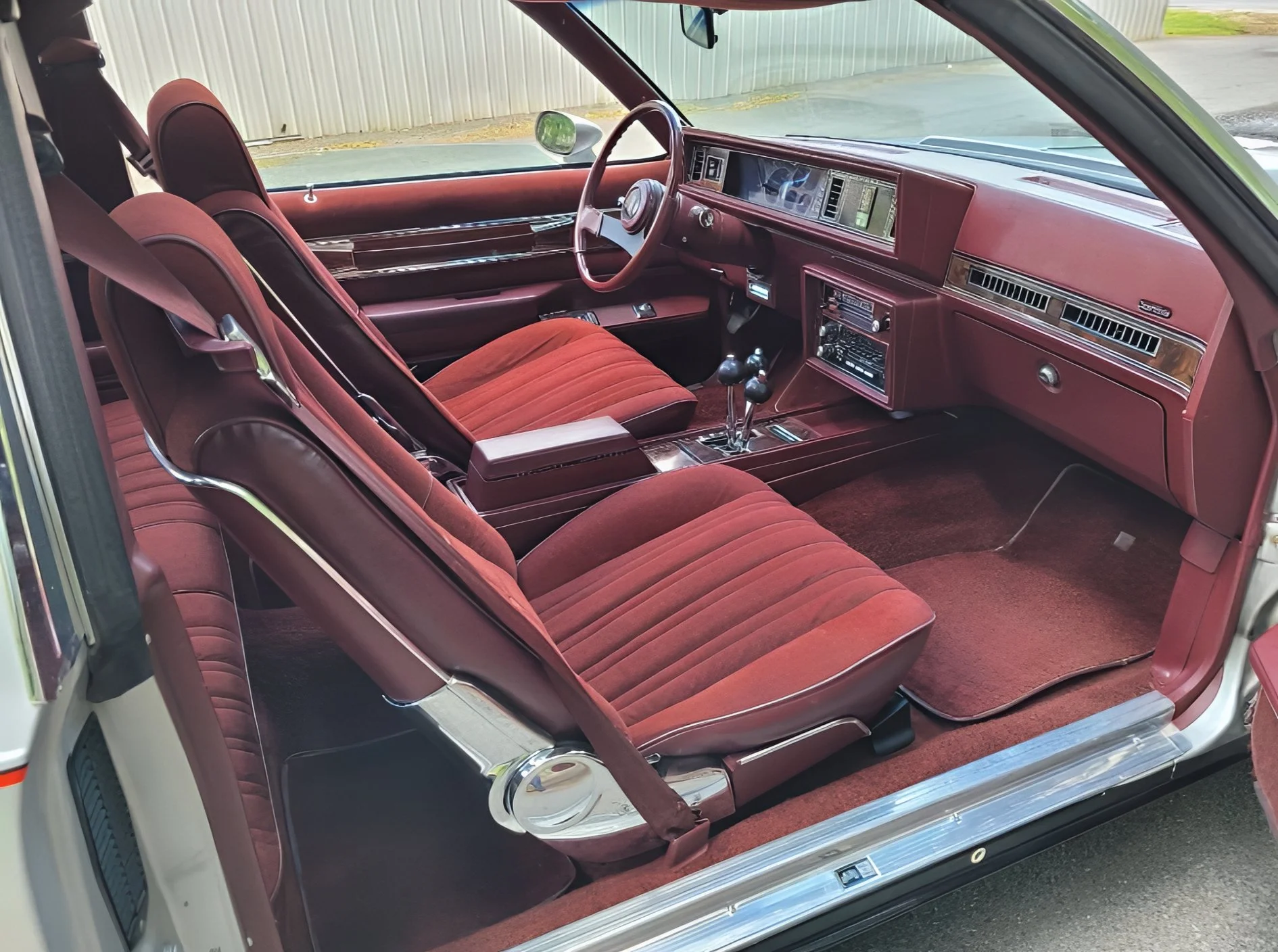 The interior of a vintage car with red velvet seats, a matching dashboard, and manual gear shifters, viewed from the passenger side.