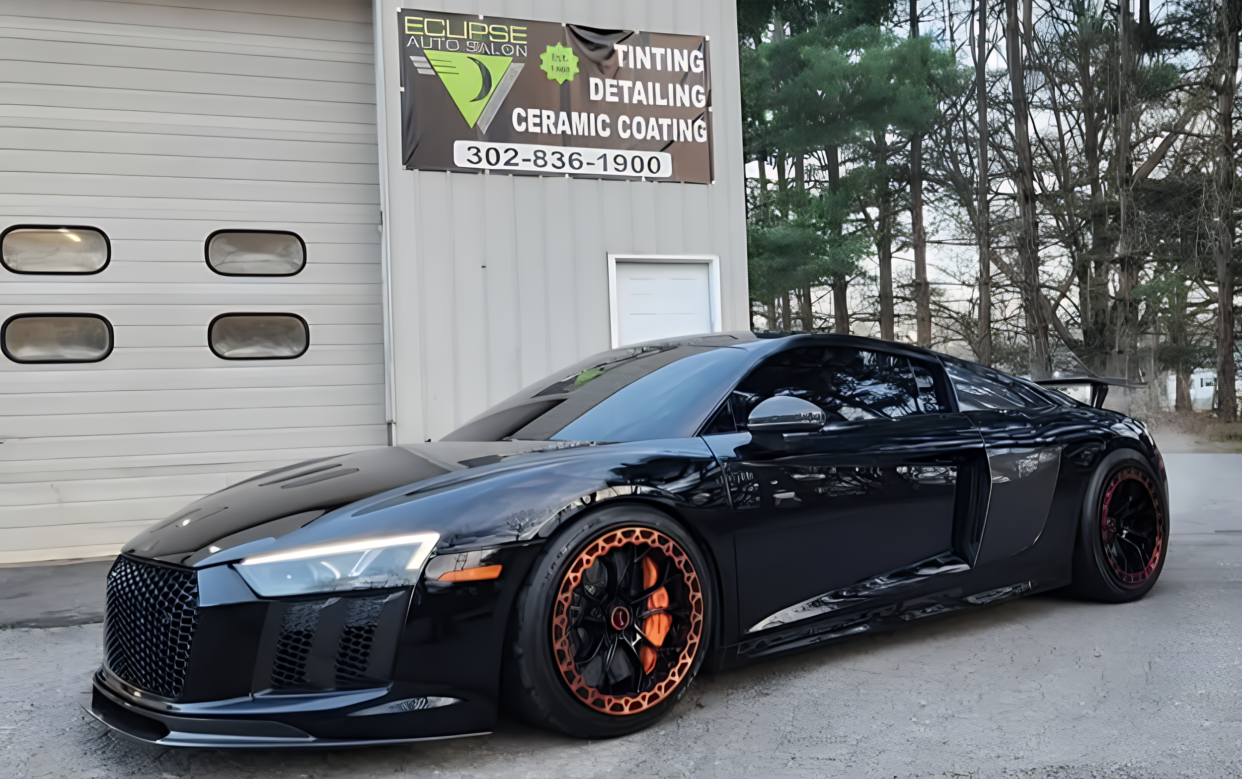 Black Audi R8 sports car parked outside an auto shop with a sign that reads 'Eclipse Auto Salon' offering tinting, detailing, and ceramic coating services.