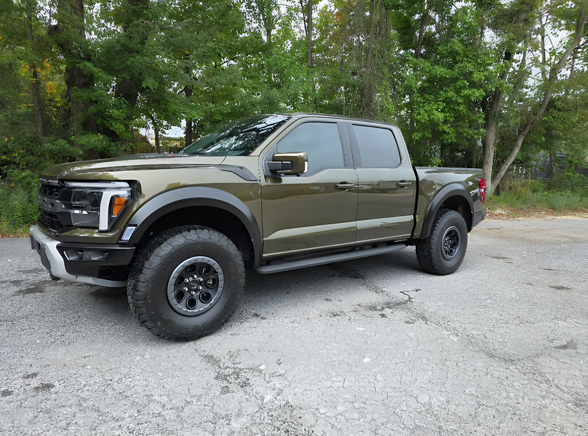 Green pickup truck parked on a gravel road with trees in the background.