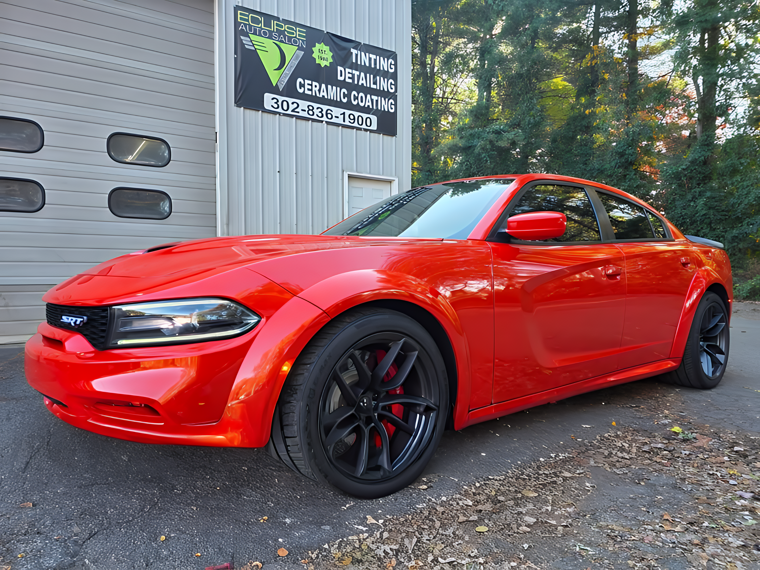 Red sports coupe parked outside a building with a sign that reads 'Eclipse Auto Salon' offering tinting, detailing, and ceramic coating services.