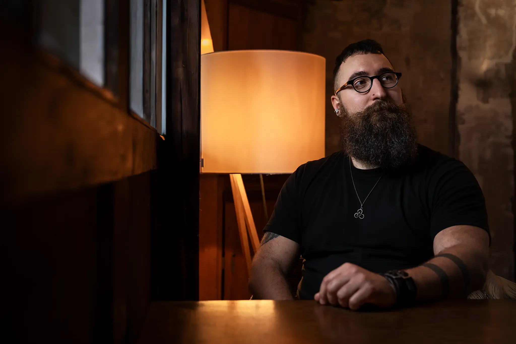 Der Künstler Nils Peter sitzt an einem Tisch in einem Raum mit Holzwänden und einer Lampe im Hintergrund.
