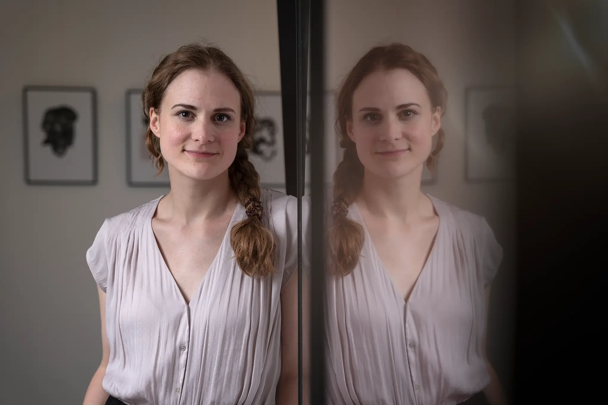 Porträt der Leiterin der VHS Bergisch Gladbach. Im Hintergrund sind drei Kunstwerke von Gesichtsporträts an der Wand sichtbar.