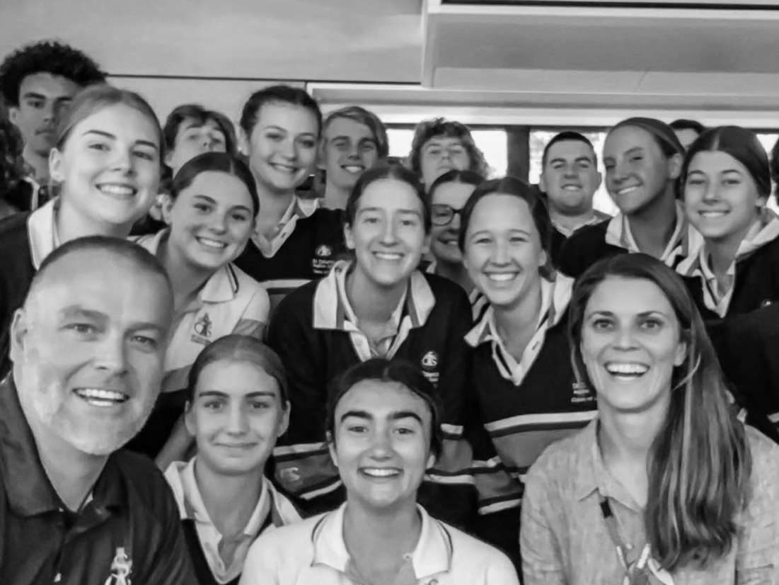 Group of students and two adults taking a selfie indoors, all smiling, with a window in the background.