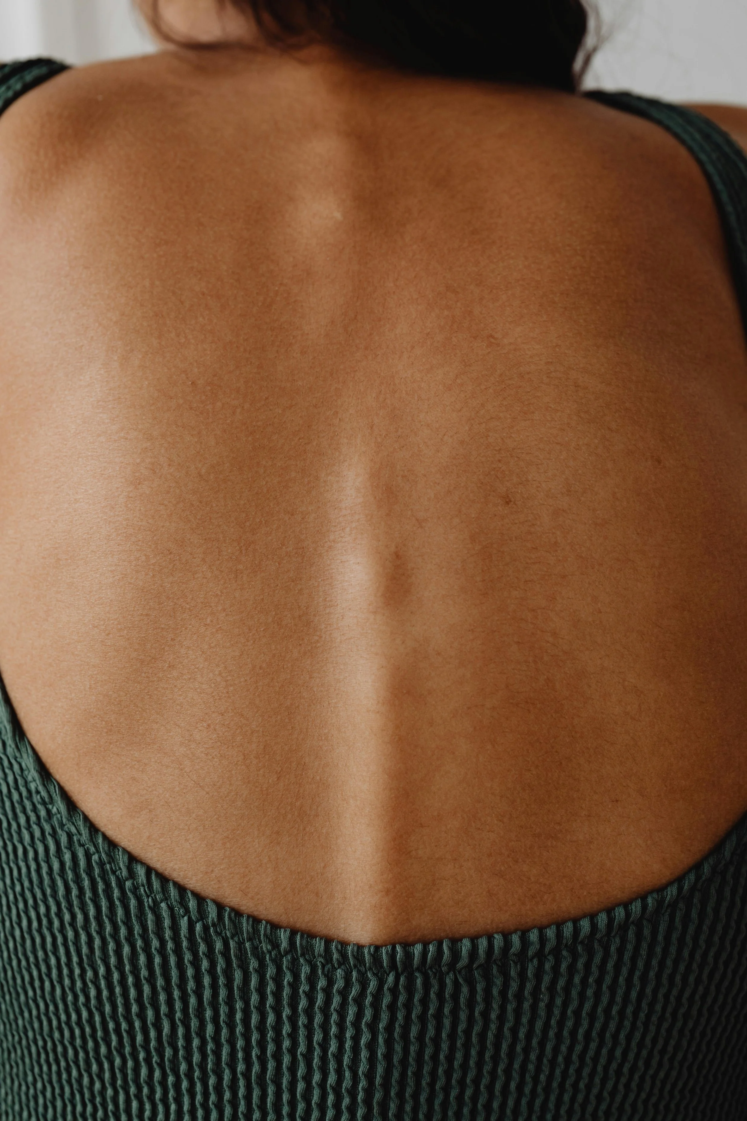 Close-up of a person's back showing smooth skin and a visible spine, wearing a ribbed green top.