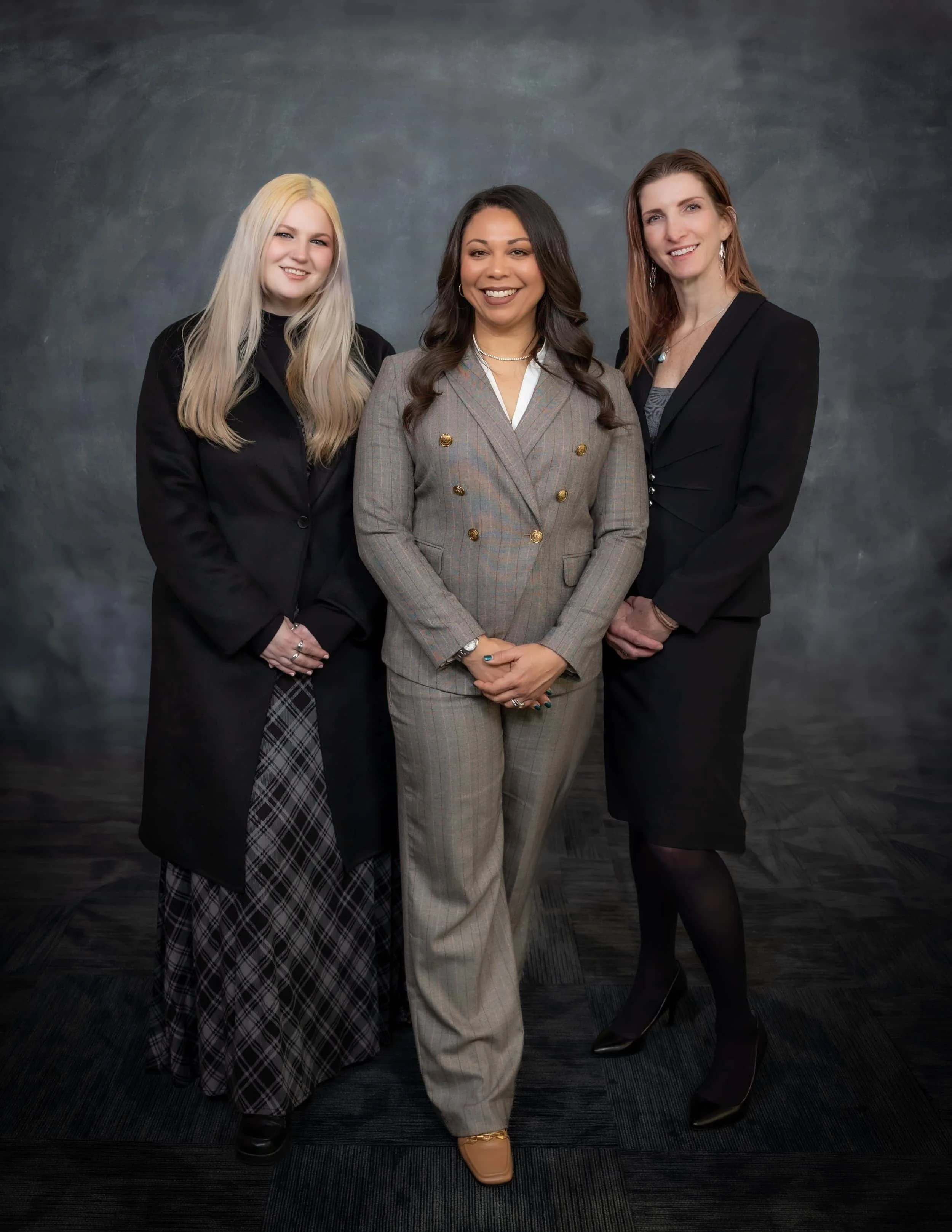 Three female legal professionals from Trestle Law posing together in business attire against a textured dark backdrop.