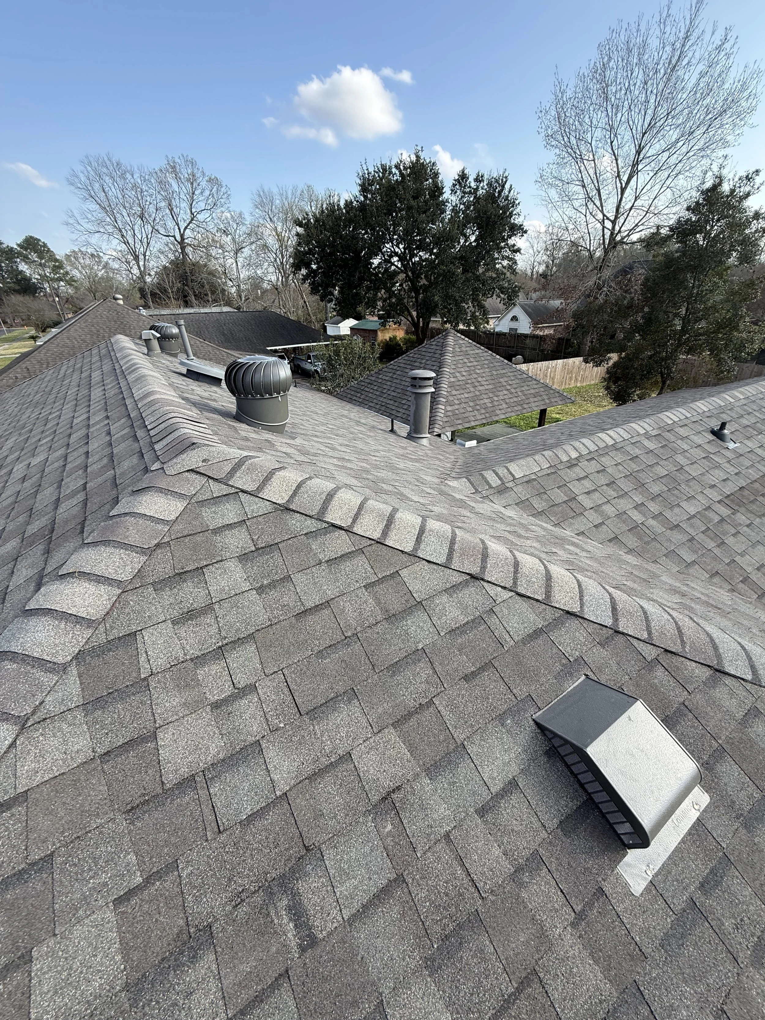 White house with brown metal roof and porch, situated on a small waterfront lot with trees in the background.