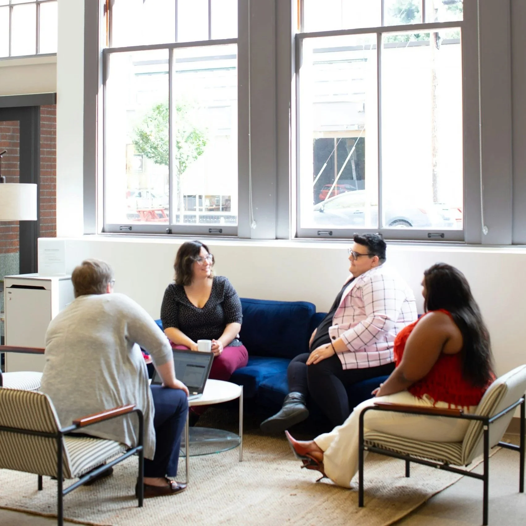People sitting and talking in a room with large windows and a hanging light fixture.