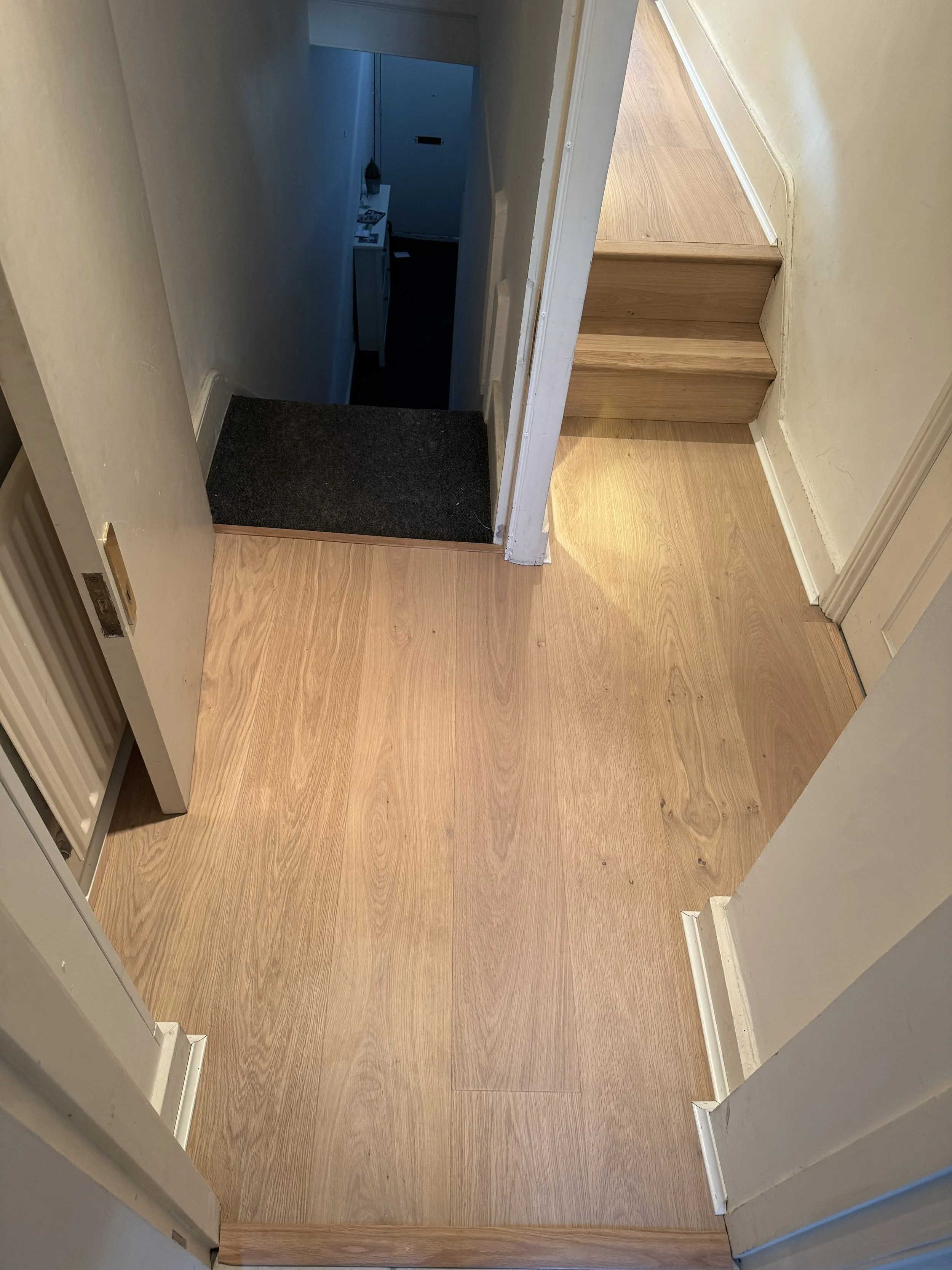 View of a small upper-floor area with wooden flooring and a staircase leading down, with a hallway visible at the bottom of the stairs.