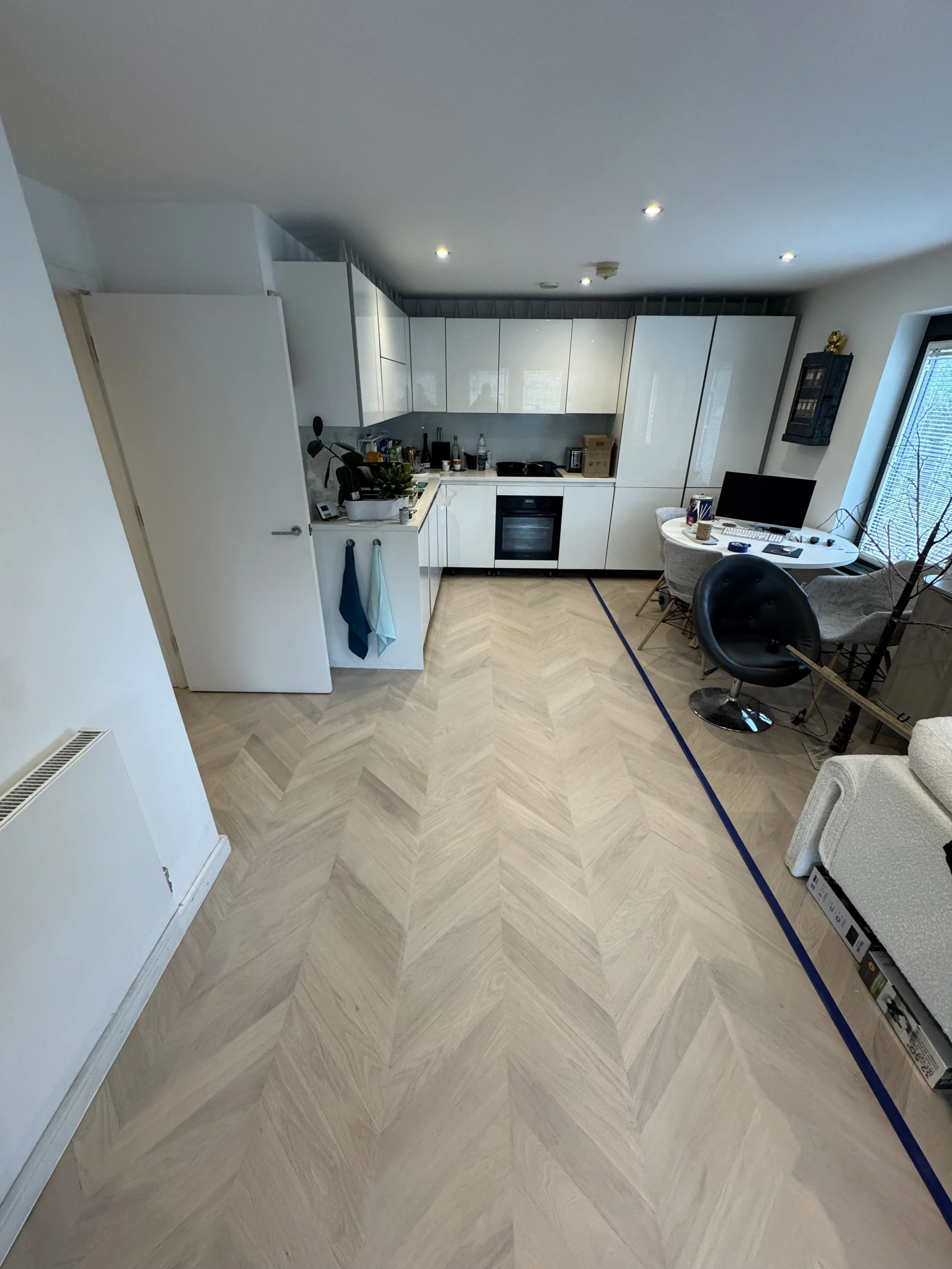Open-concept kitchen and dining area with light wood herringbone flooring, white cabinets, and a small round dining table with chairs near a window.