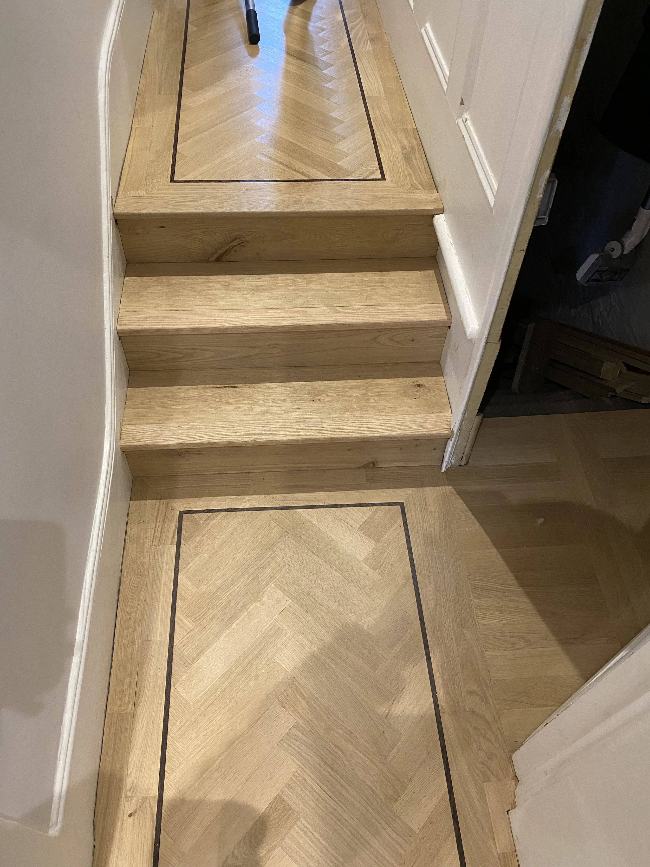 Wooden stairs leading up to a patterned wooden floor, with two steps and a black border on the floor.
