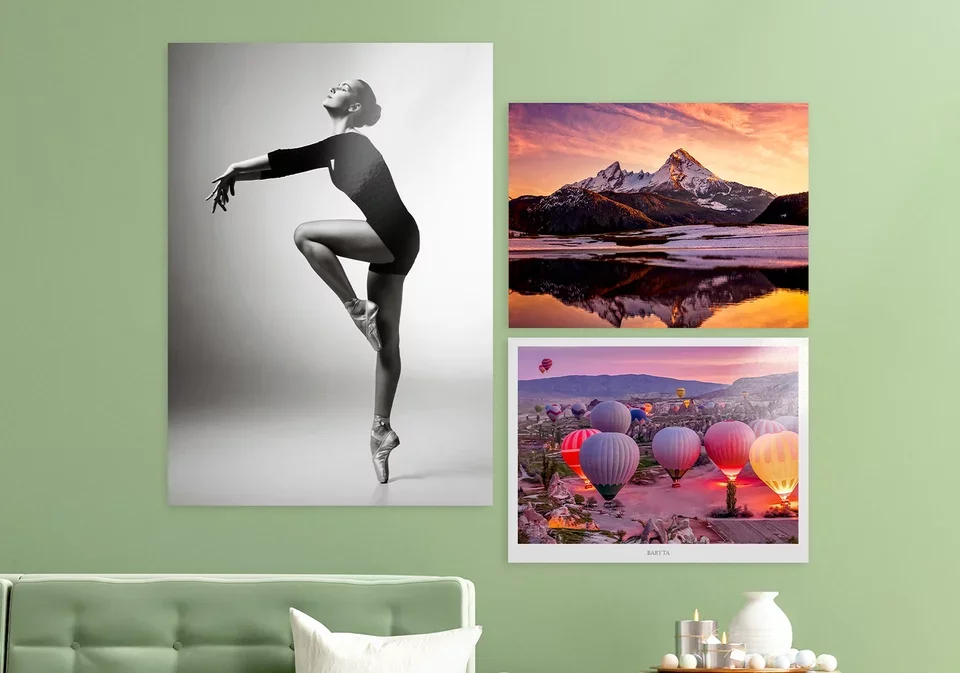 Une pièce avec un mur vert clair décoré de trois affiches, une grande noir et blanc d'une danseuse en position de ballet sur pointes, une image de montagnes au lever ou coucher du soleil, et une photo de montgolfières colorées au lever ou coucher du soleil.