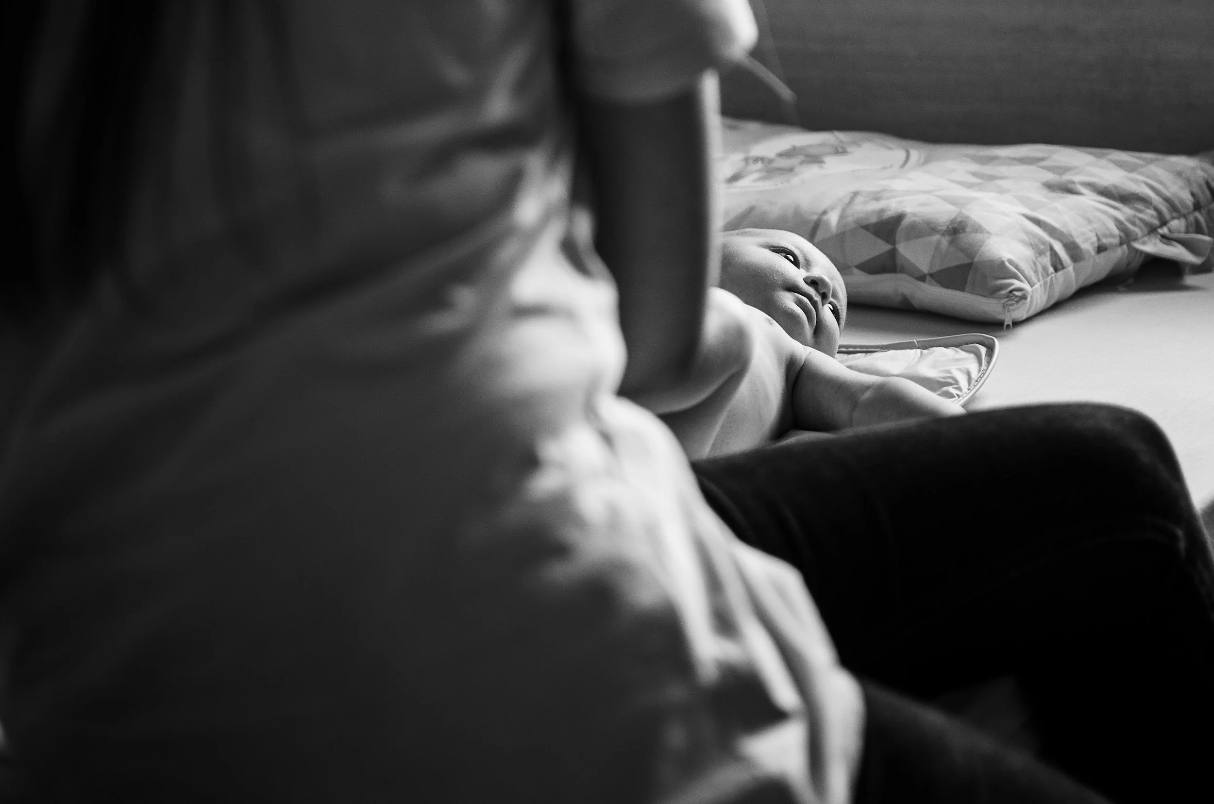 Black-and-white photo of a newborn baby lying on a bed beside an adult