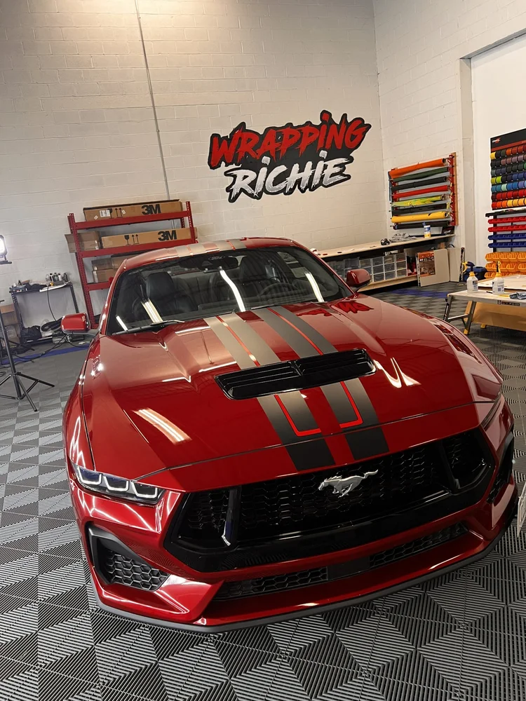 Red Mustang with racing stripes inside Wrapping Richie’s wrap shop