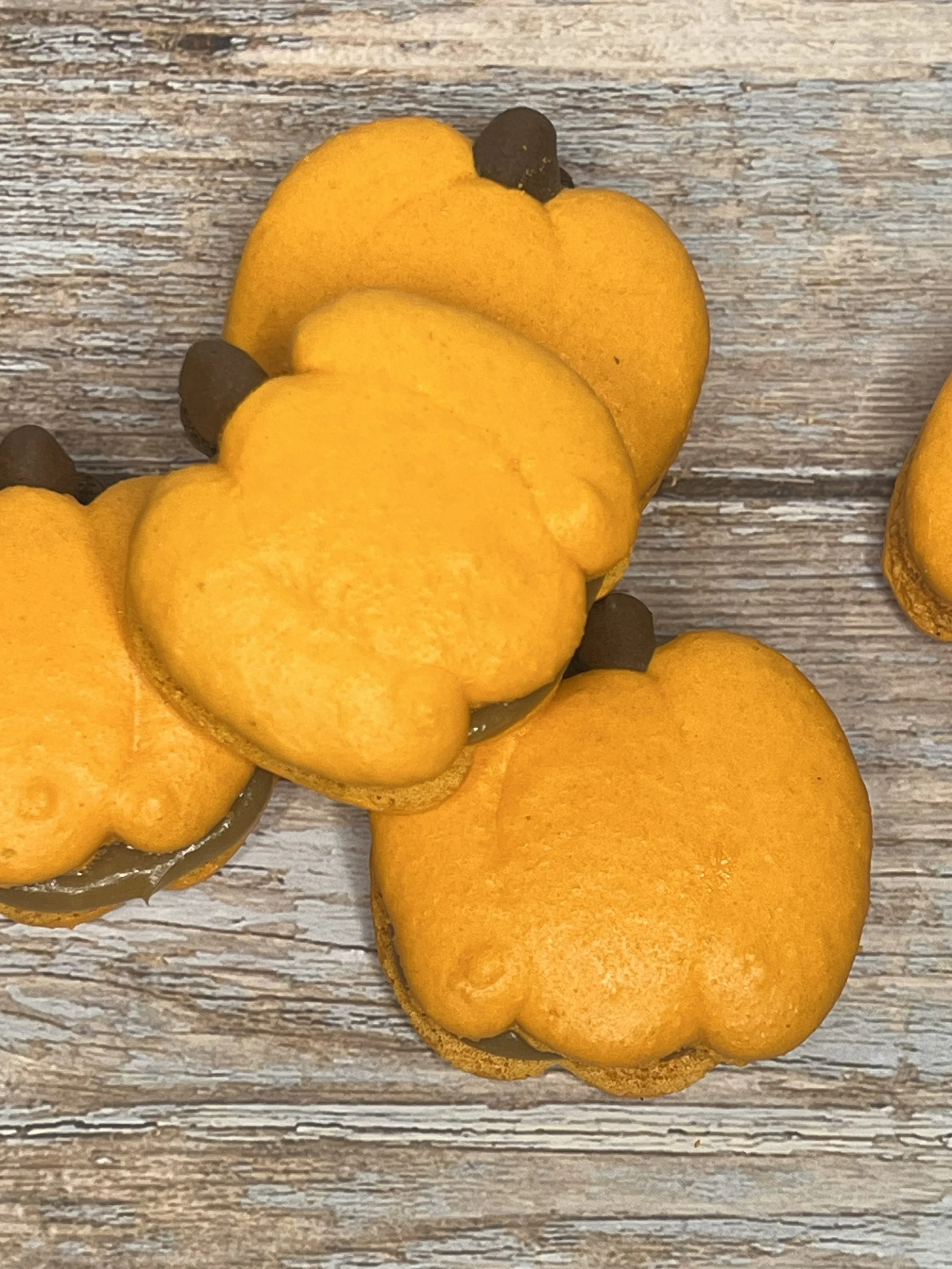Close-up of pumpkin-shaped cookies with orange icing and brown stem decorations on a wooden surface.