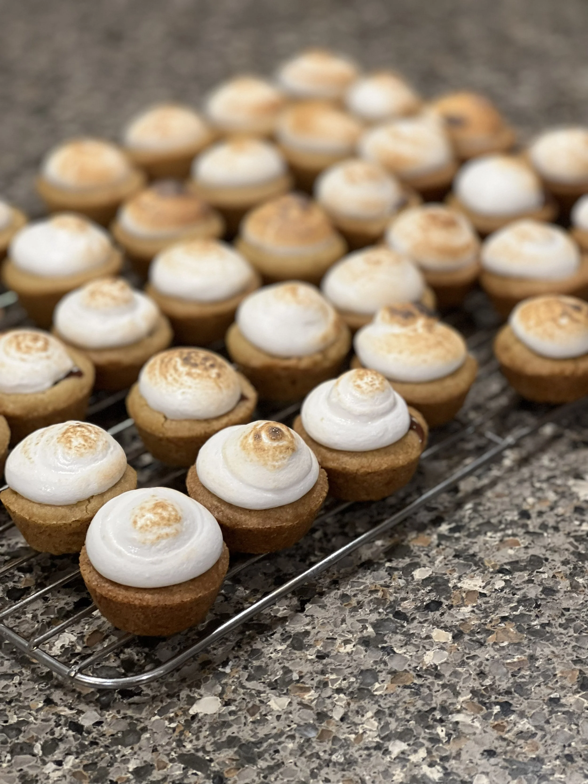 A tray of toasted mini pie or tart shells topped with toasted meringue on a kitchen countertop.