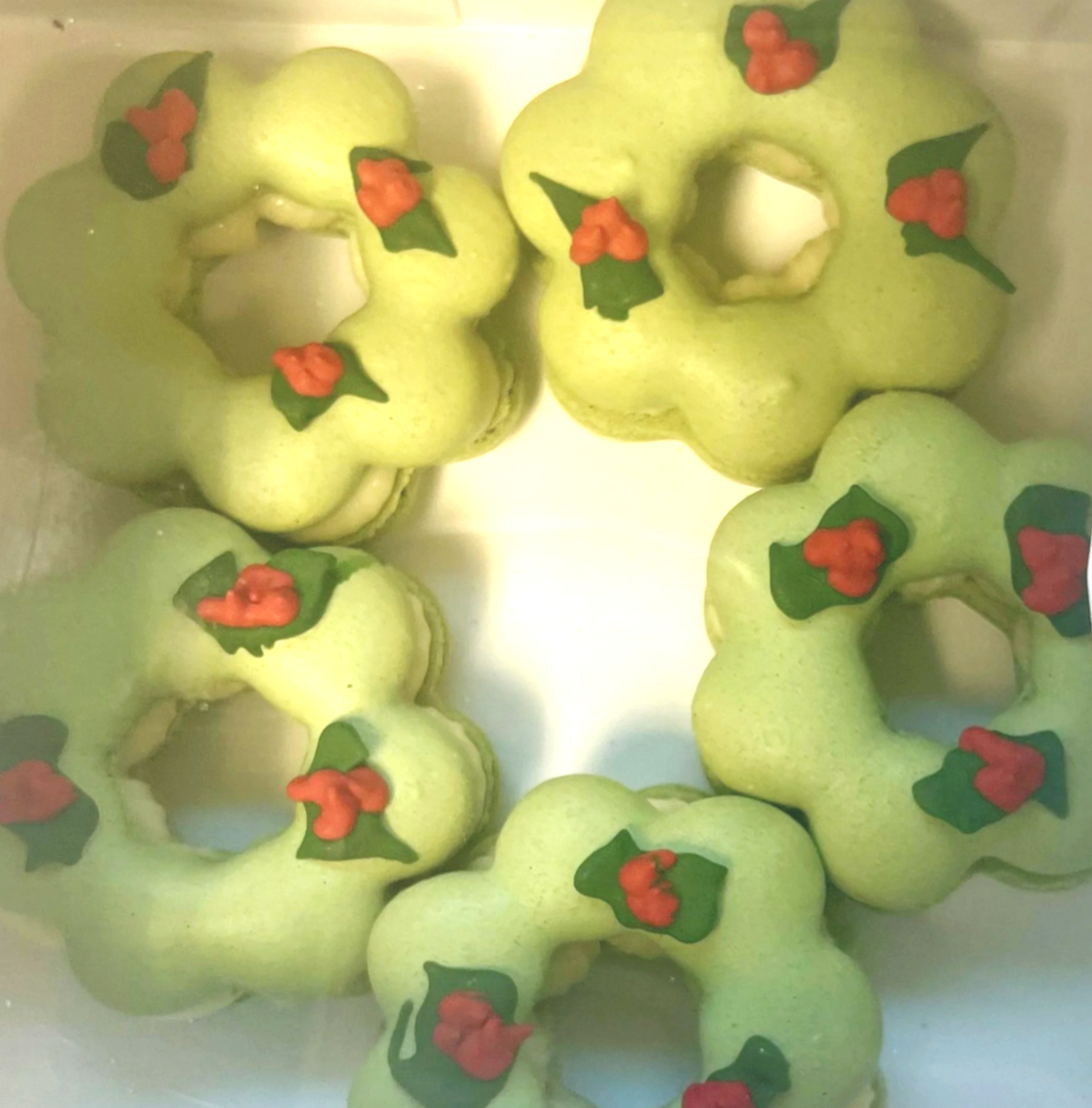 Holiday-themed green cookies decorated with holly leaves and berries, arranged in a circle.