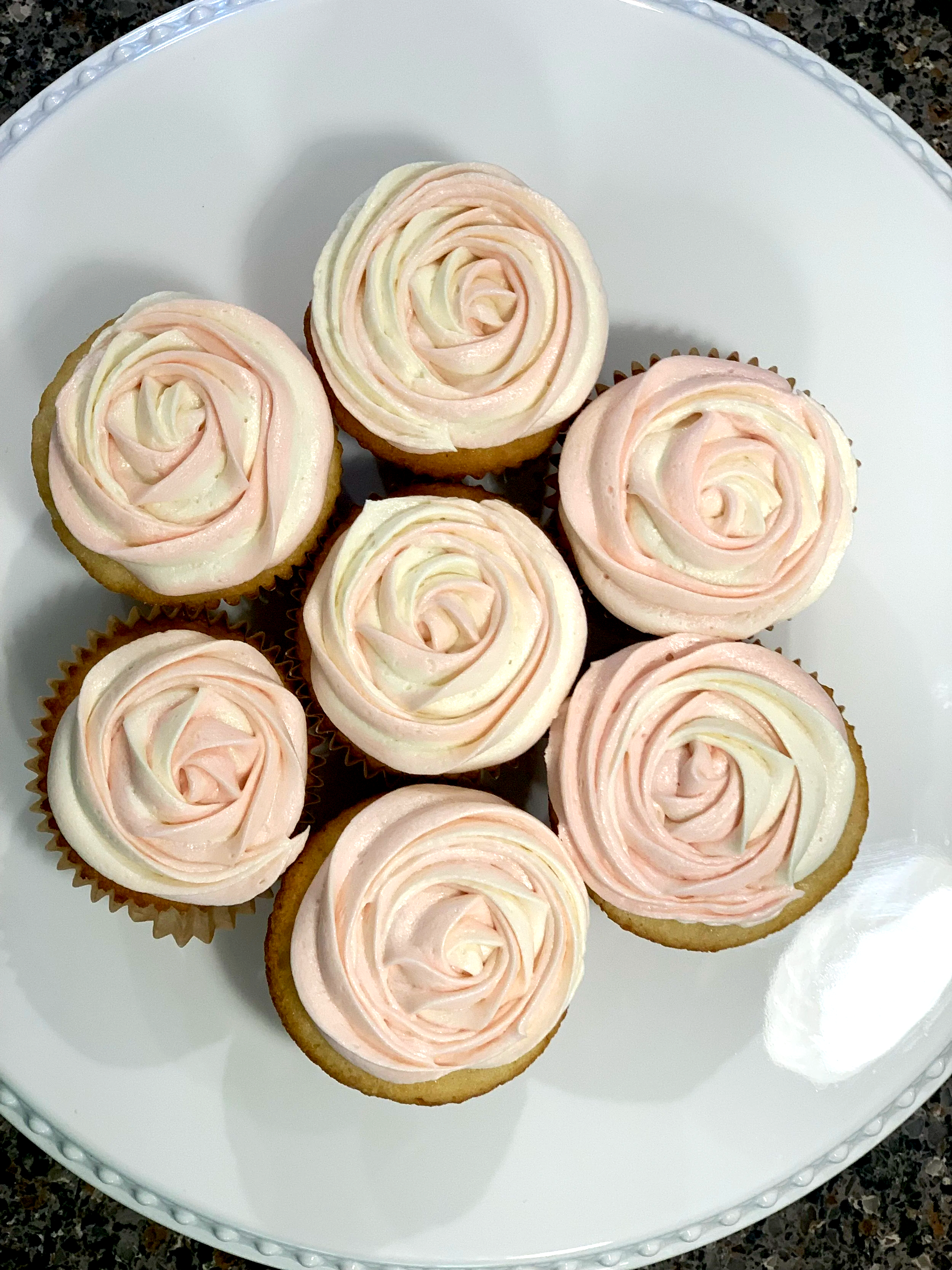 Nine cupcakes with pink and white rose-shaped frosting on a white plate.