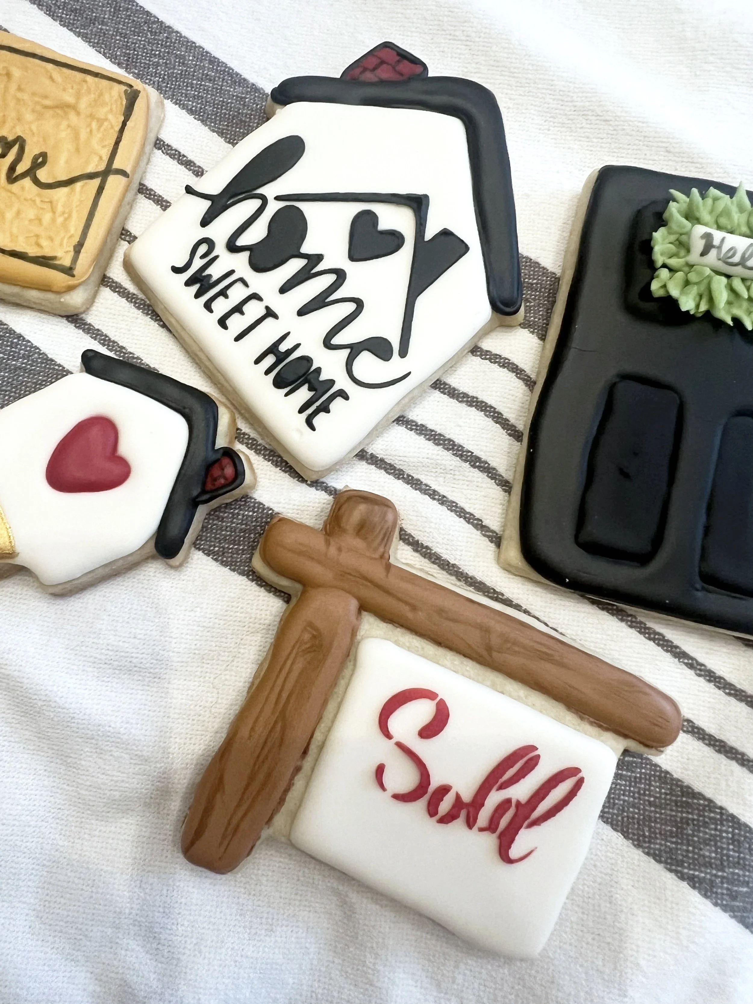 Decorative cookies with messages and symbols including a house with the words "home sweet home," a white cookie with a red heart and black graduation cap, a wooden hammer, and other decorated cookies.