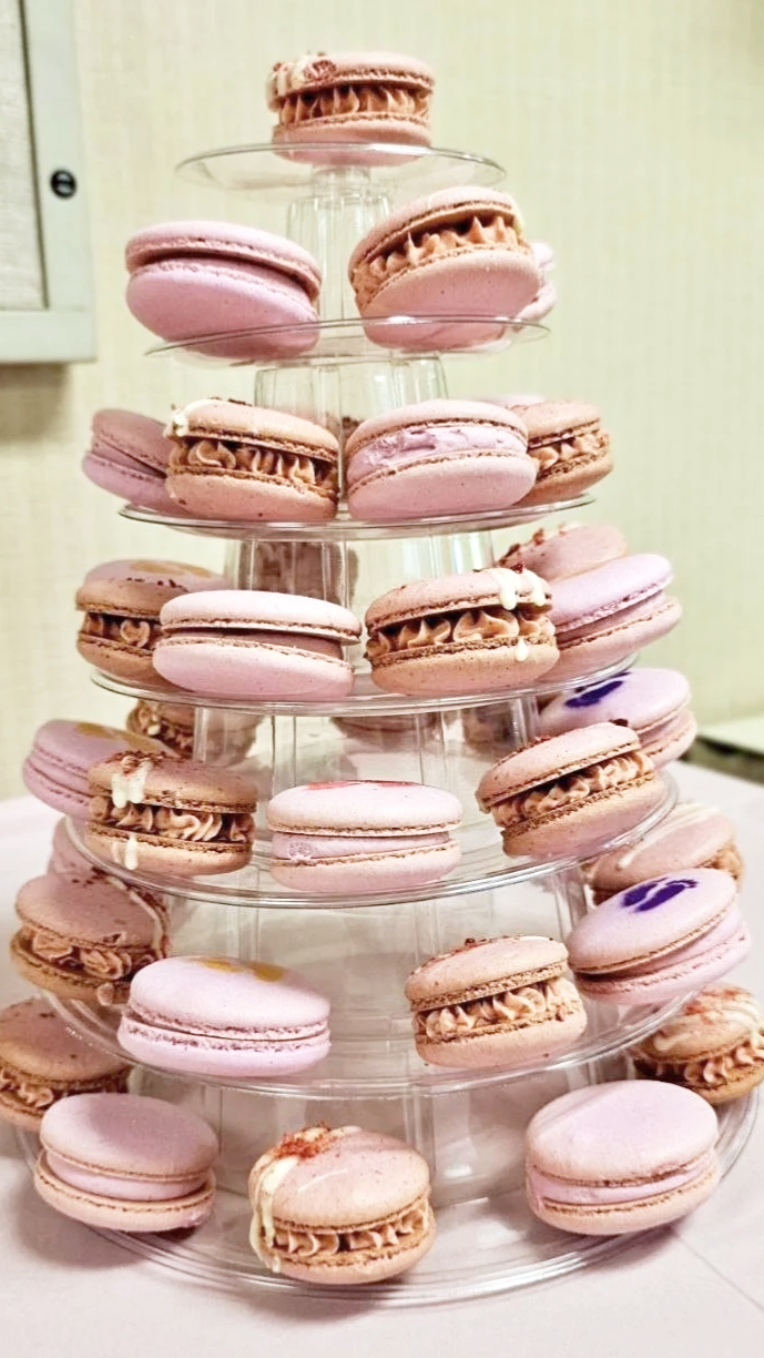 Pink and brown macarons arranged on a multi-tiered clear acrylic stand for display or serving.
