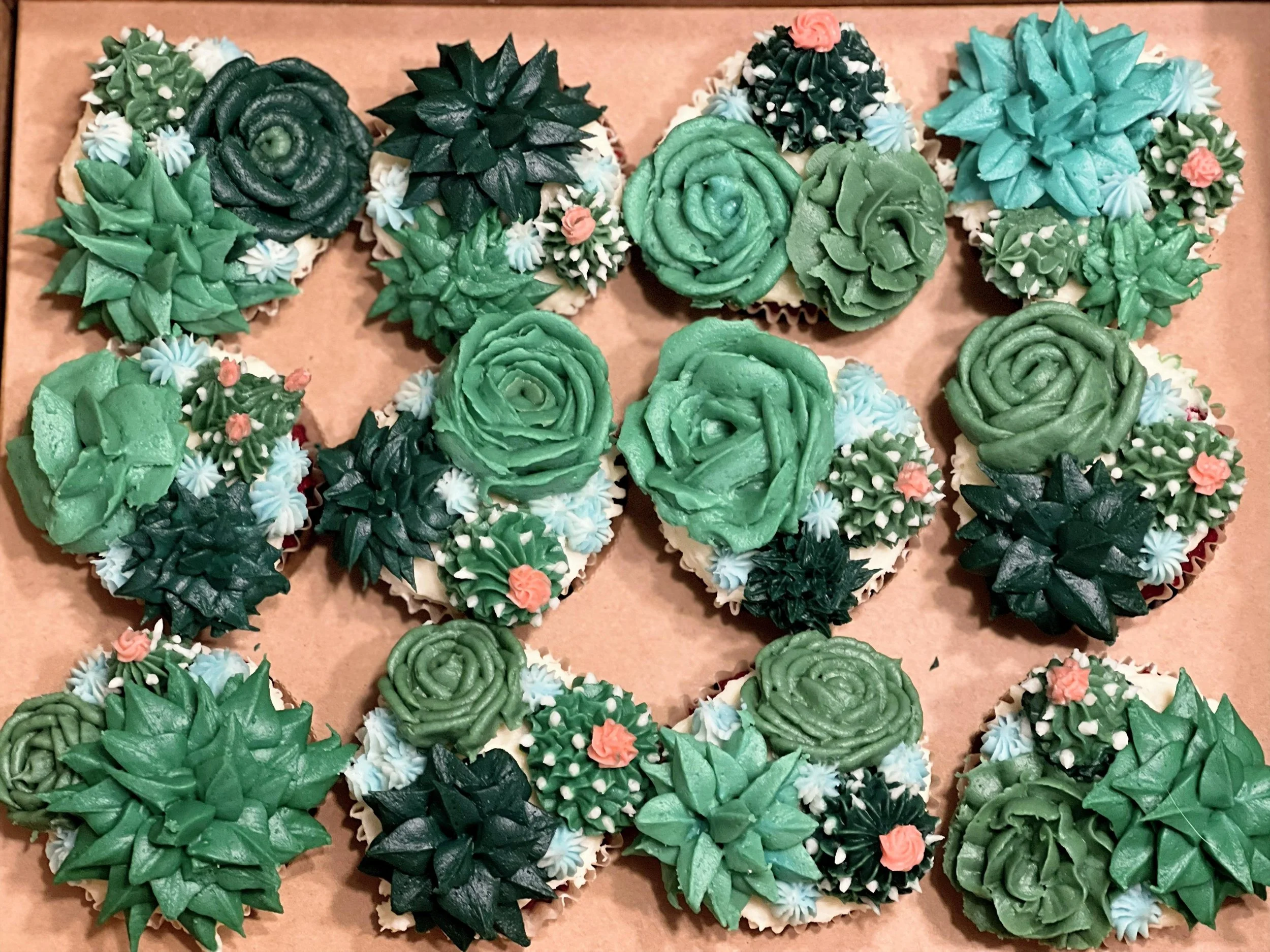 Cupcakes decorated with green and dark green succulent-shaped frosting, with small pink and white floral accents.