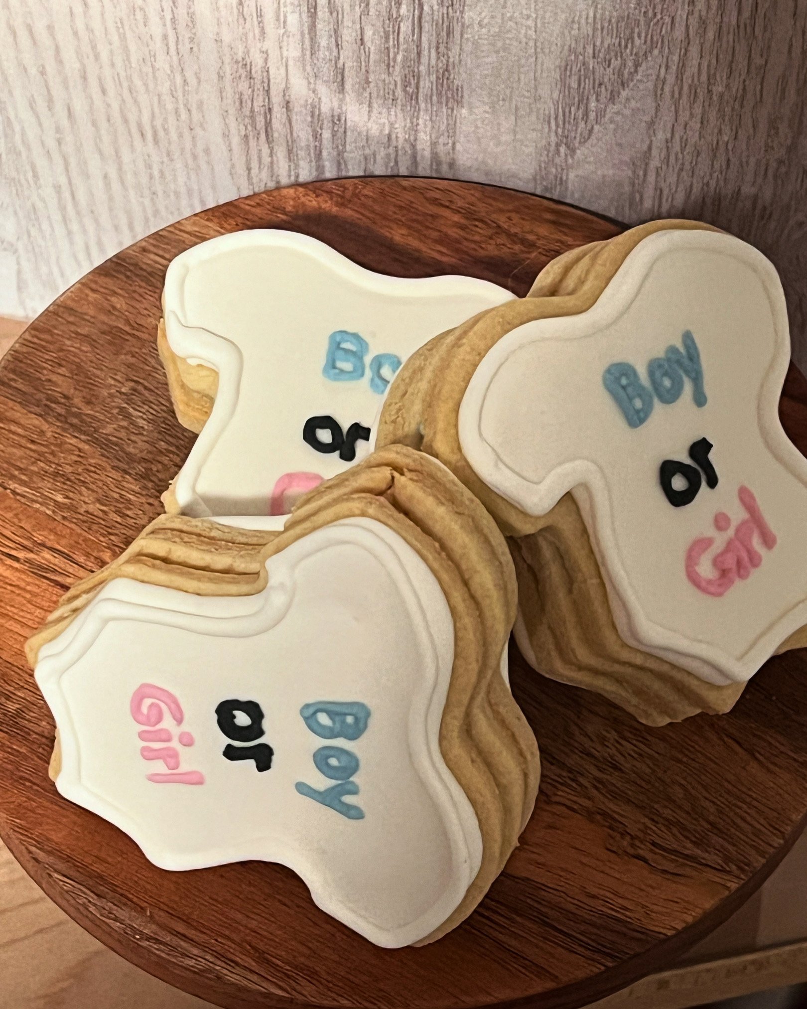 Cookies with white icing decorated with the words "Boy or Girl" written in blue and pink icing, placed on a wooden surface.