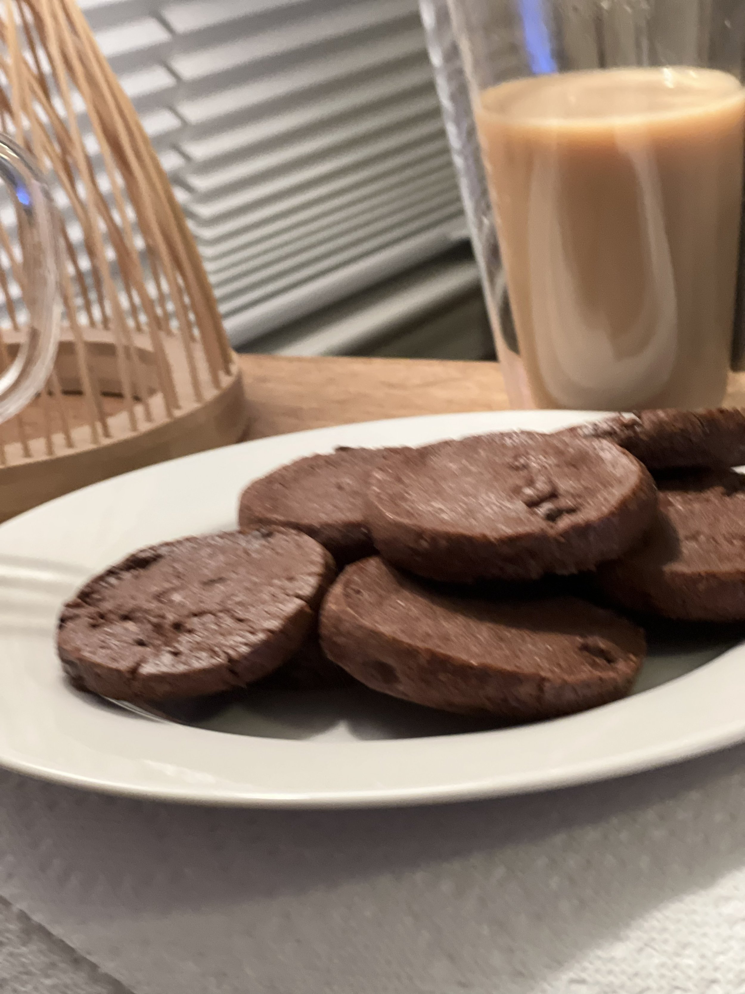 Plate of chocolate cookies with a glass of iced coffee or iced latte in the background.