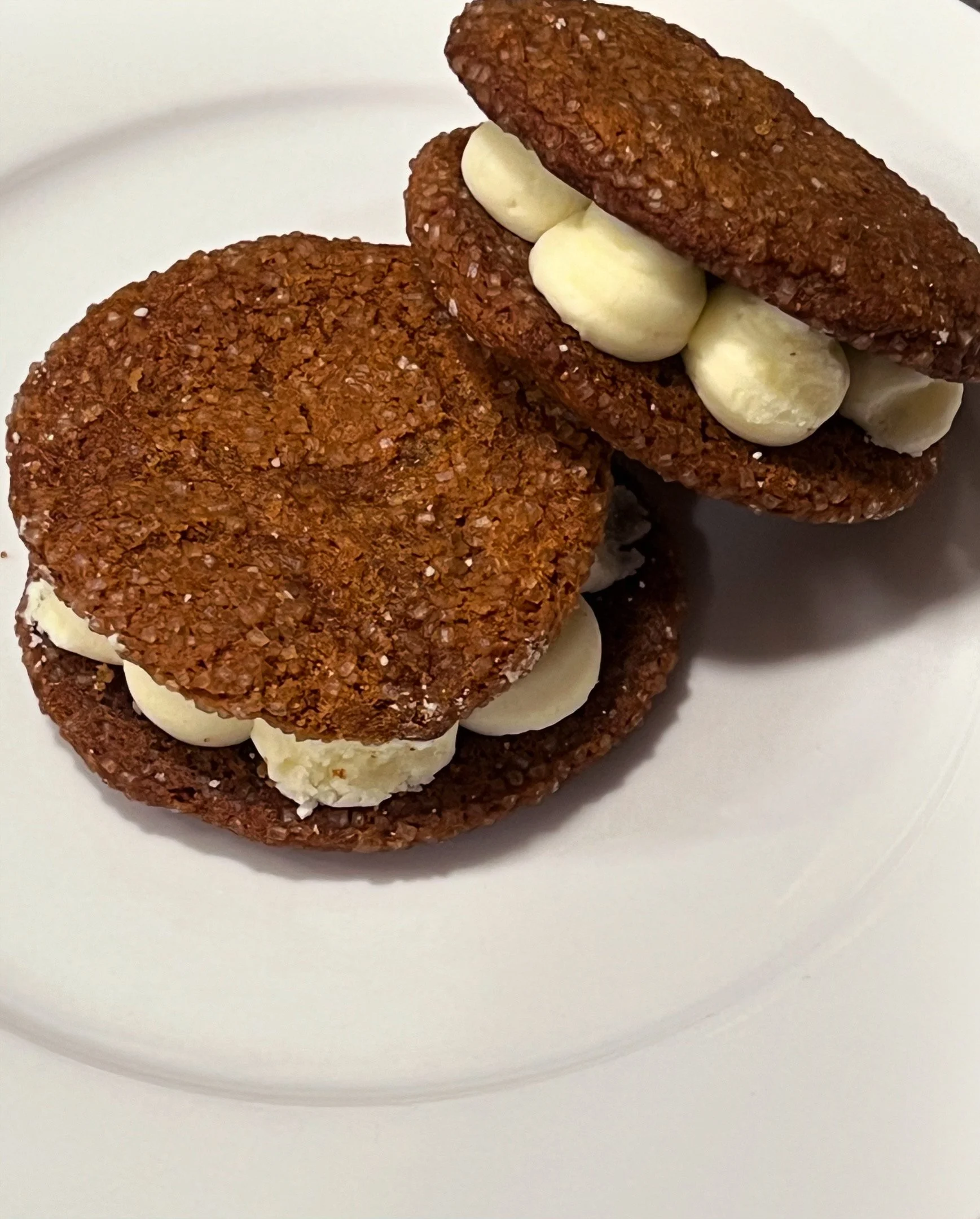 Two cookies with a cream filling on a white plate.
