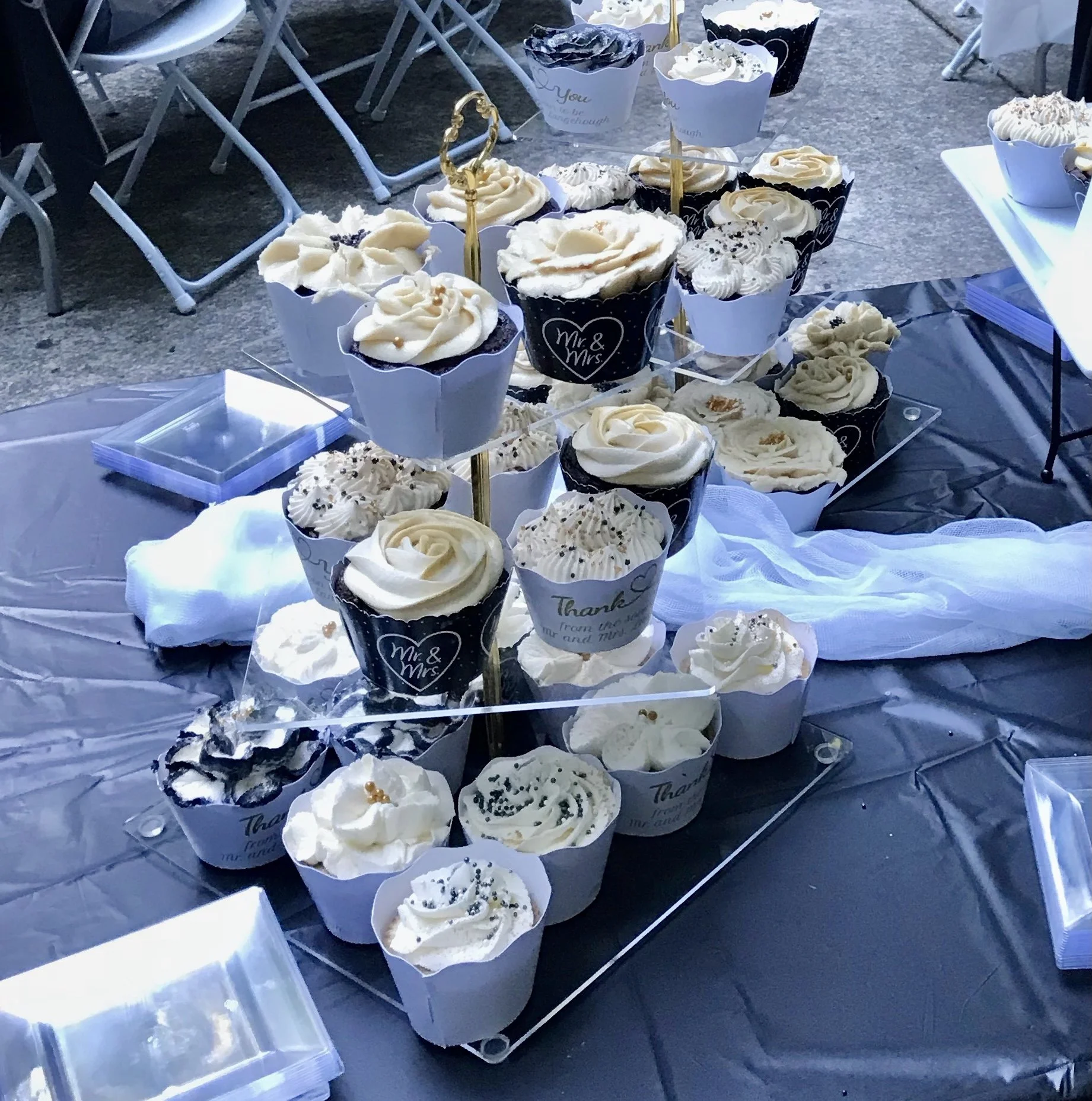 A display of decorated cupcakes at a celebration, with some labeled as 'Mr. & Mrs.' and 'Thank you,' featuring white frosting and various sprinkles.