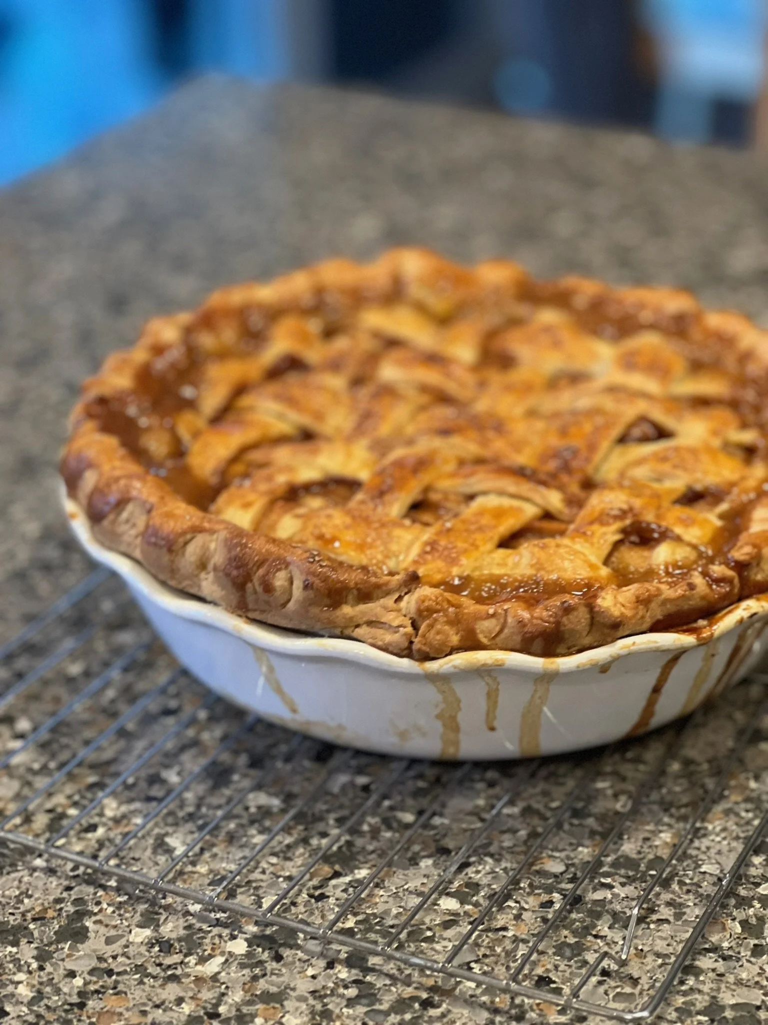A freshly baked apple pie with a lattice crust sitting on a cooling rack on a speckled countertop.