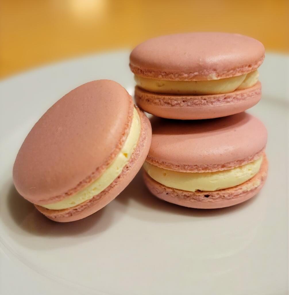 Three pink macarons with cream filling on a white plate