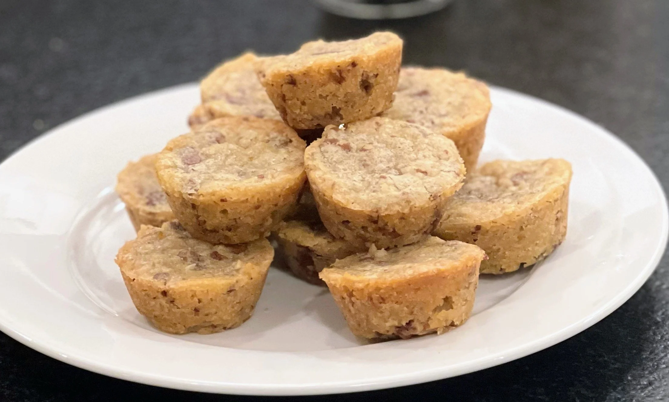 Plate of chocolate chip cookie dough bites stacked on a white plate against a dark background.