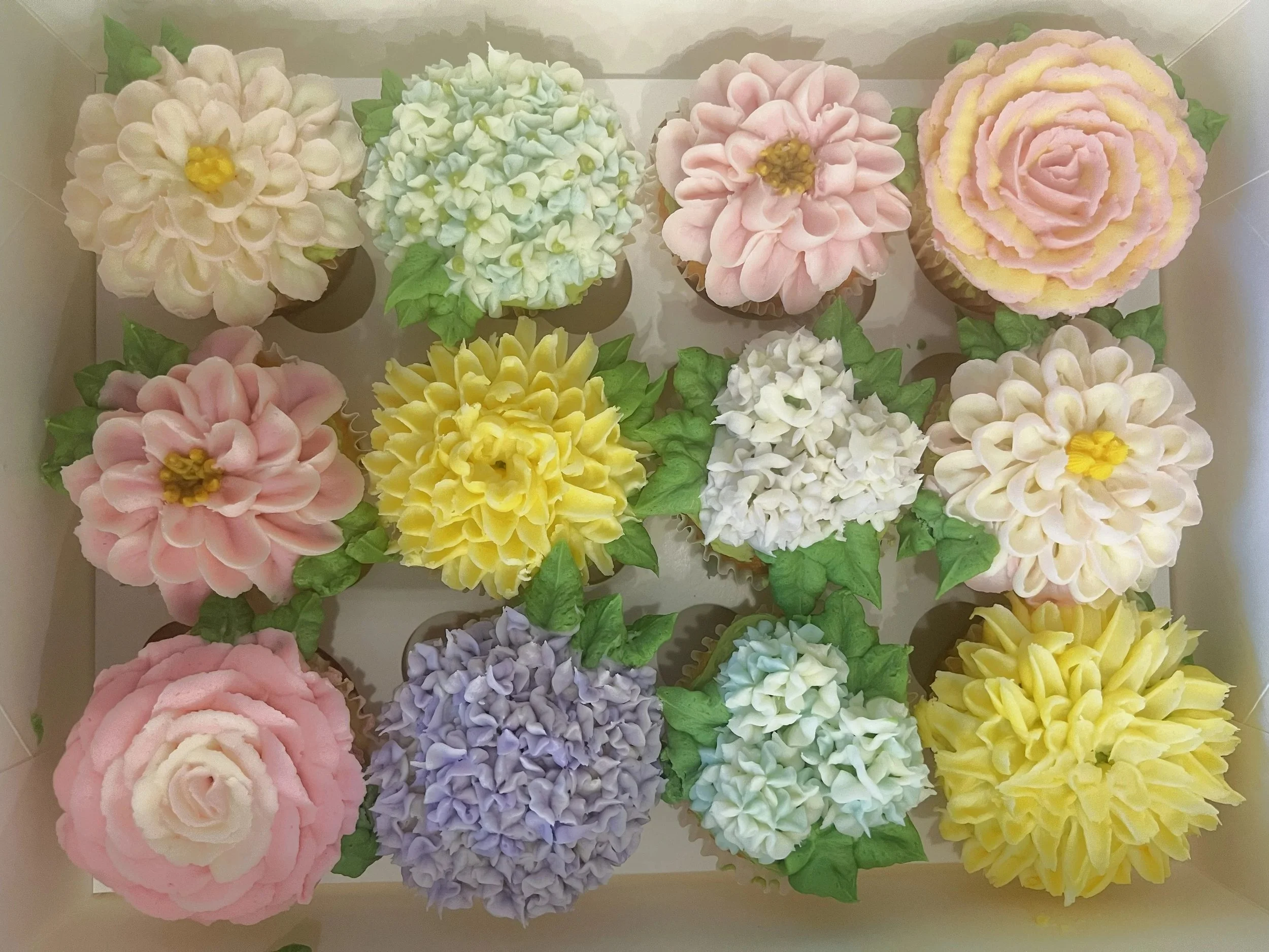 A dozen cupcakes decorated as different types of flowers.