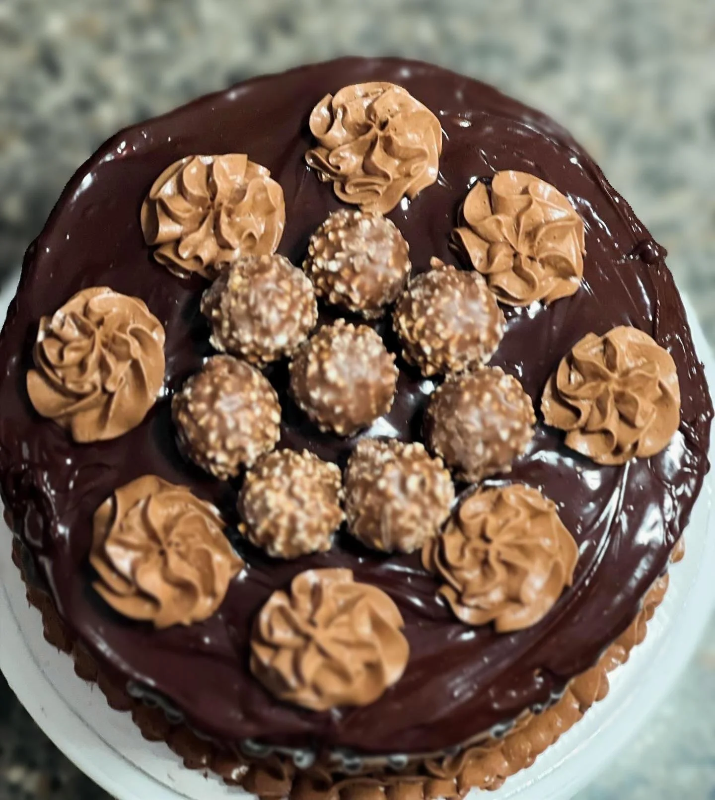 Chocolate cake decorated with rosettes of chocolate frosting and topped with Ferrero Rocher chocolates in the center.