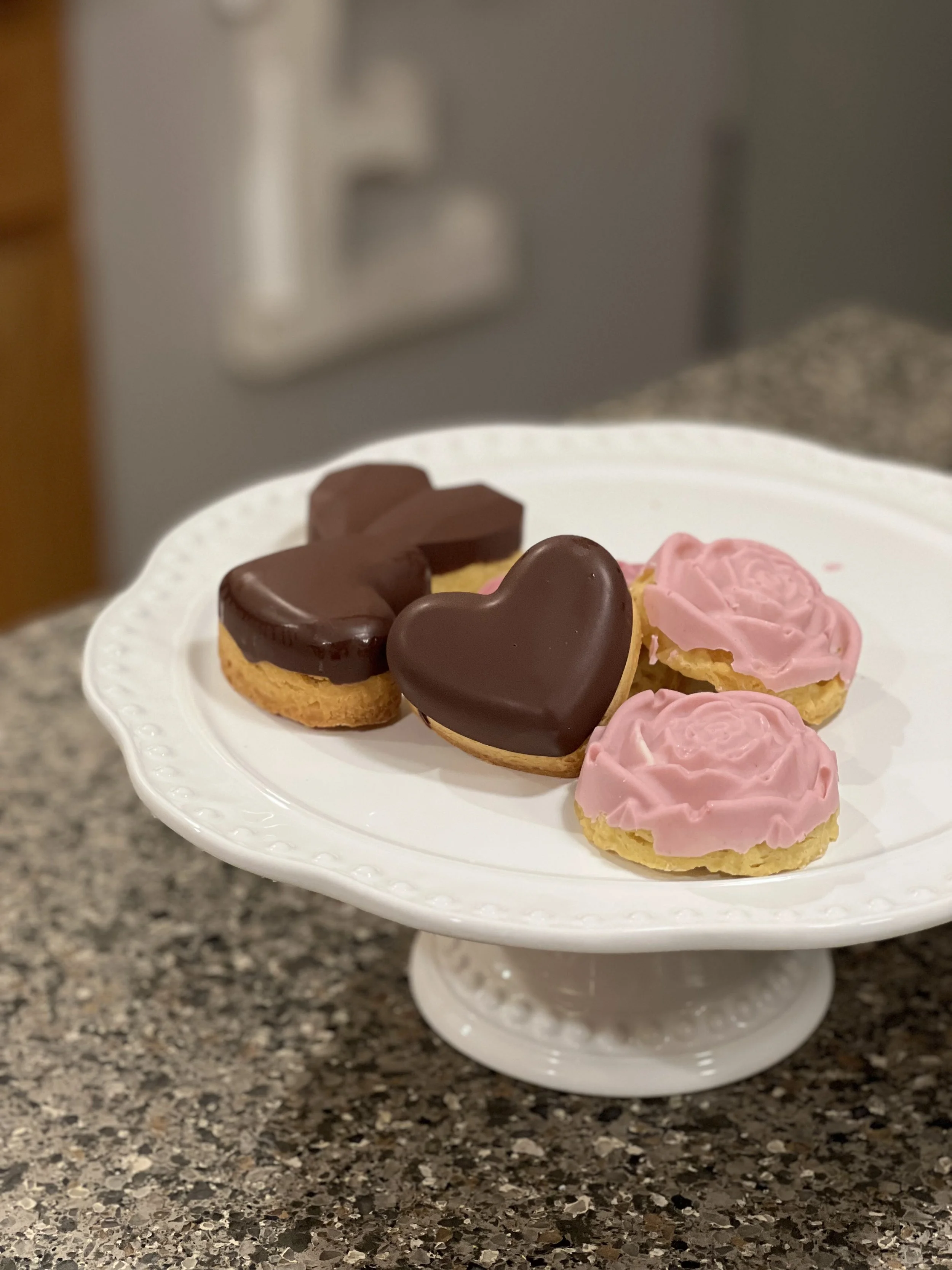 Heart-shaped sugar cookies with pink and chocolate icing on a white cake stand.