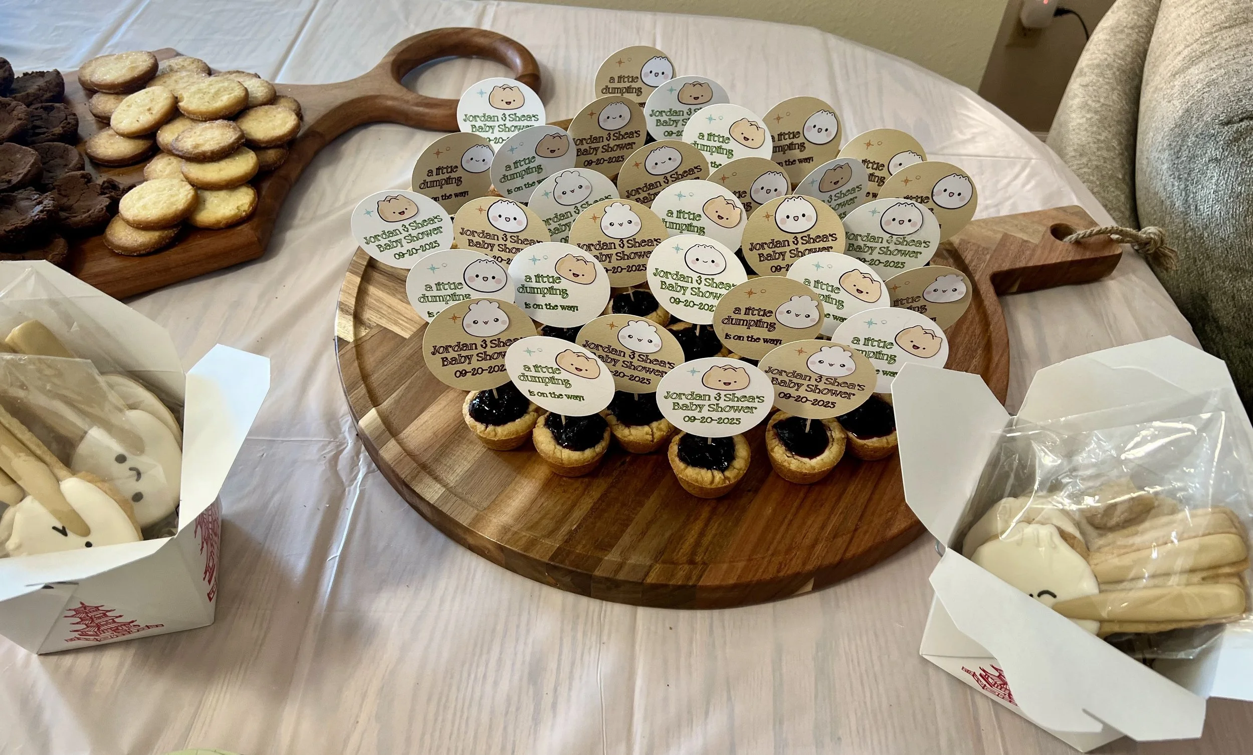 Cupcakes with animal face toppers, cookies in a box with animal designs, and assorted cookies on a cutting board, all displayed on a table for a baby shower.
