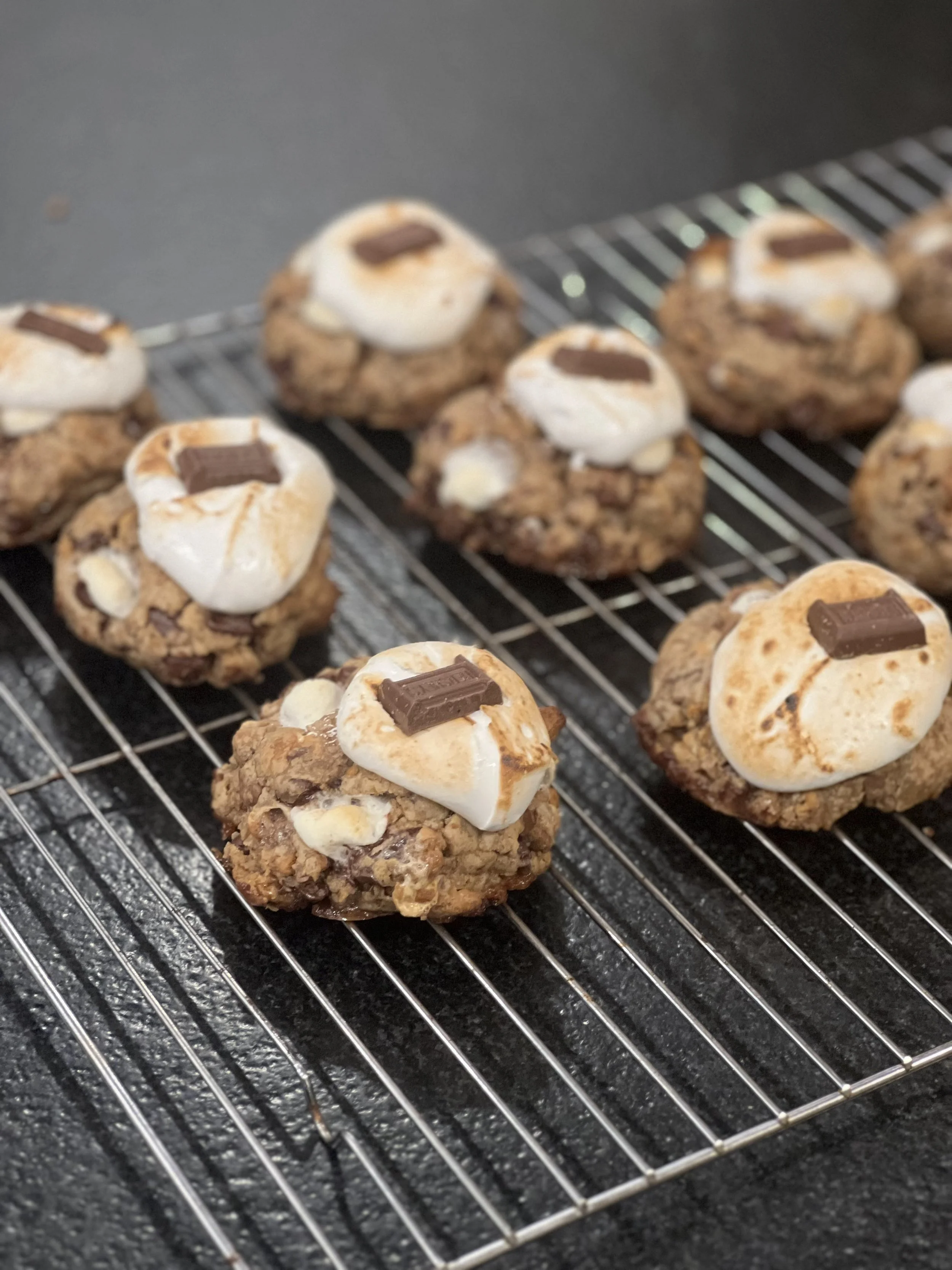 Cookies topped with roasted marshmallows and pieces of chocolate on a cooling rack.